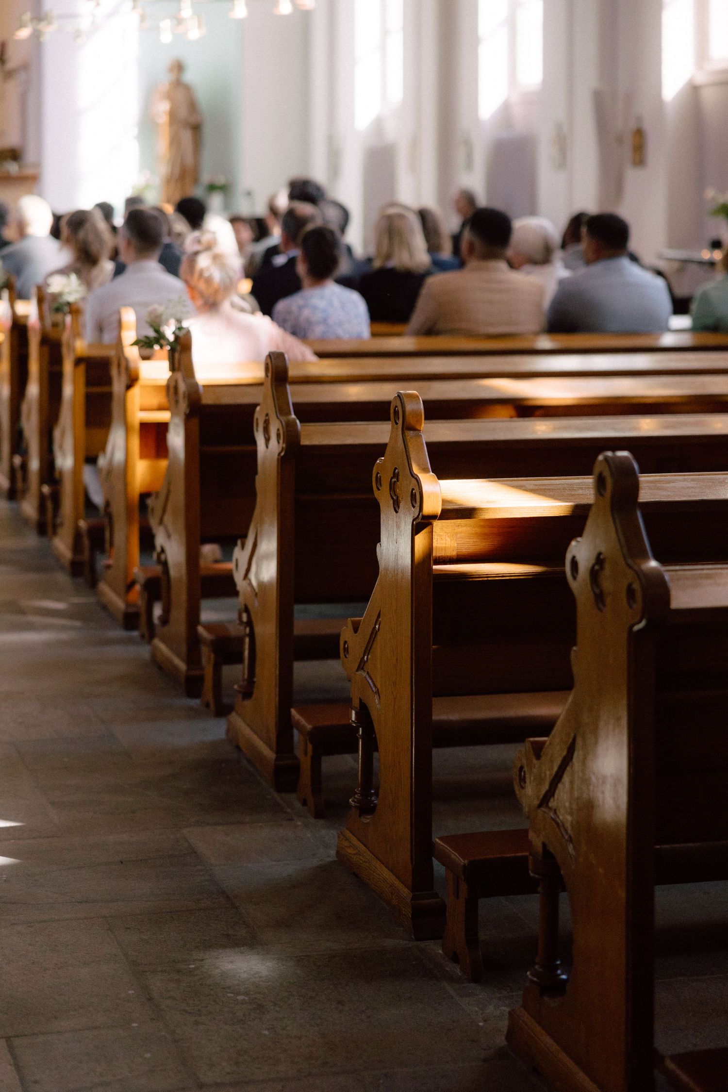 Sunlit church interior showing empty wooden pews with natural lighting streaming through windows.