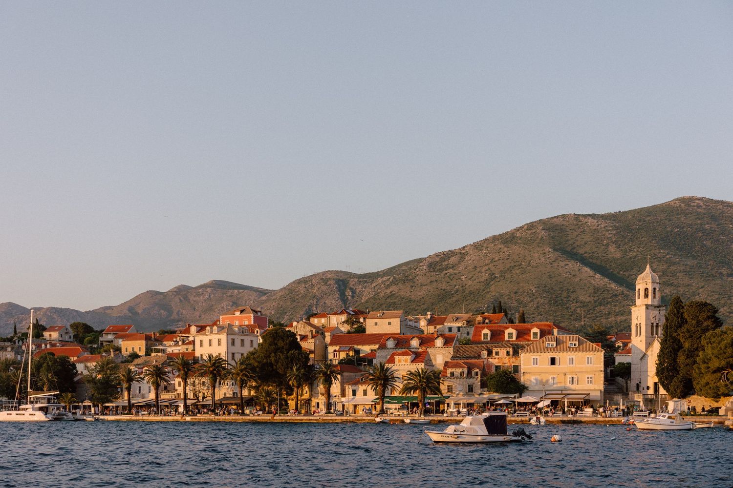 Coastal Mediterranean village with terracotta roofs and church tower along the waterfront.
