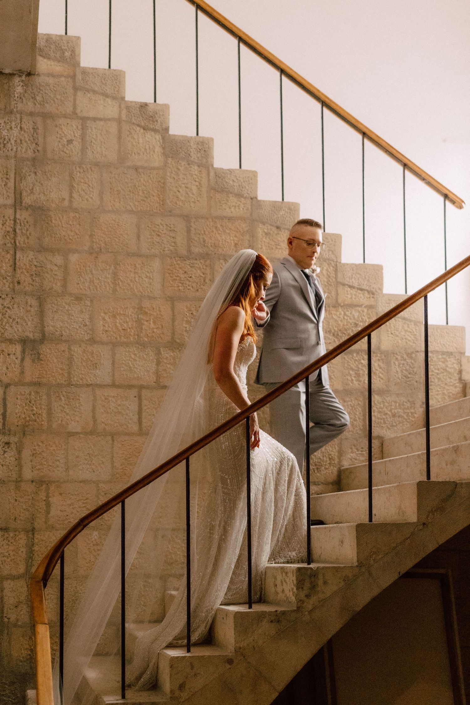Sequence of a couple ascending stone stairs with dramatic lighting and wooden handrail.