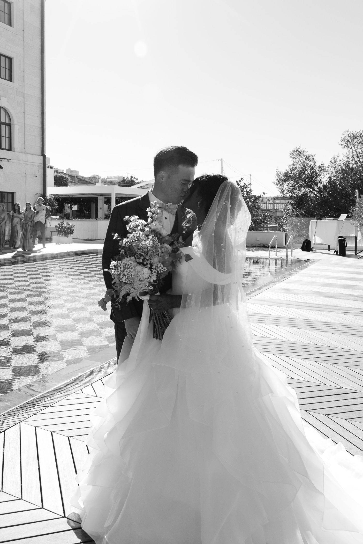 Black and white photo of bride and groom sharing a kiss outdoors near a fountain on wedding day.