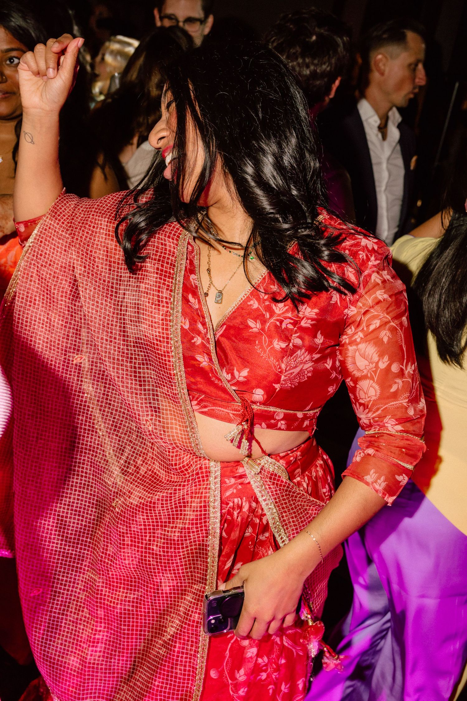 Woman dancing joyfully in elegant red floral Indian lehenga outfit at a vibrant wedding reception.