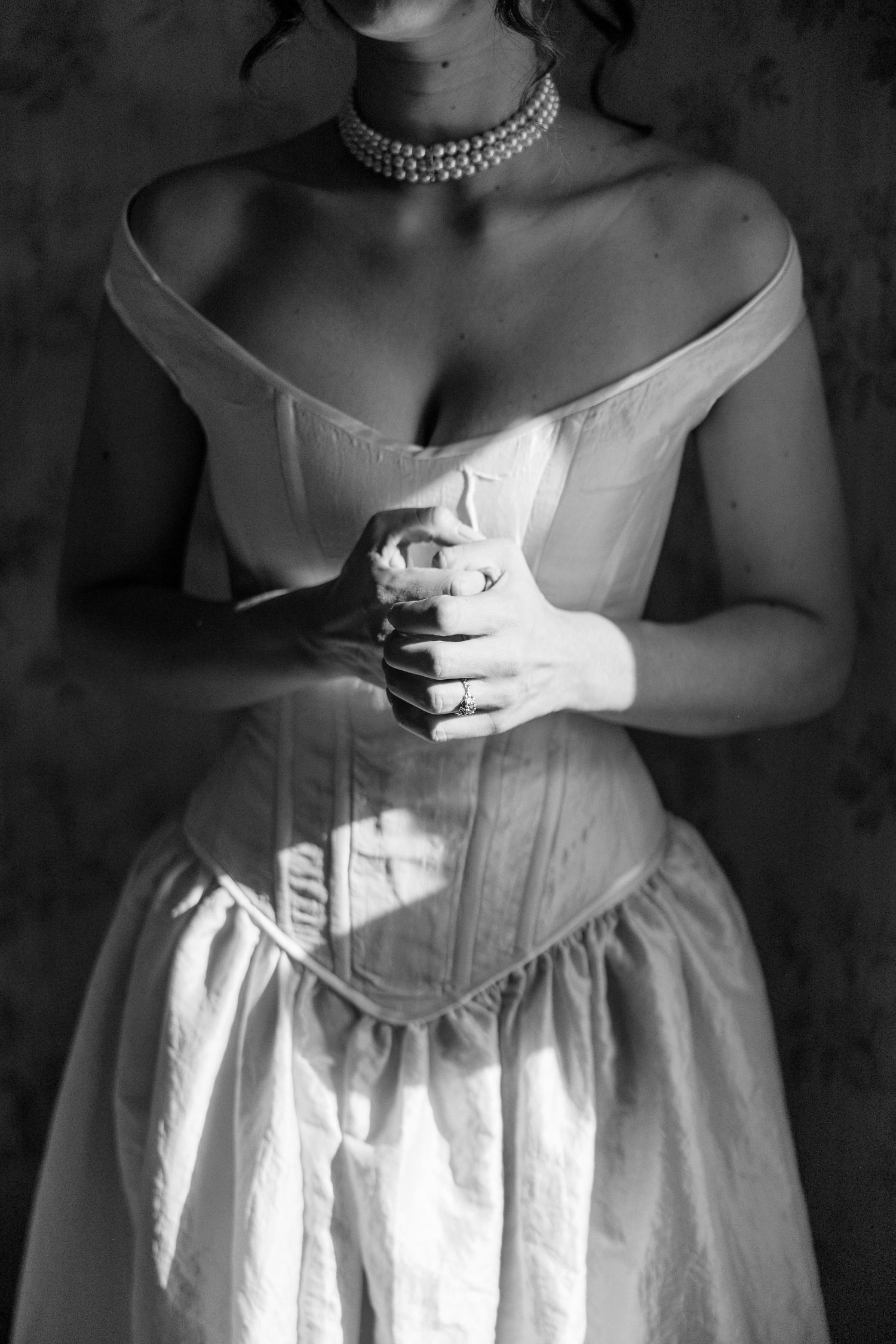 A black and white photo of an elegant wedding dress bodice with off-shoulder design and pearl choker necklace.