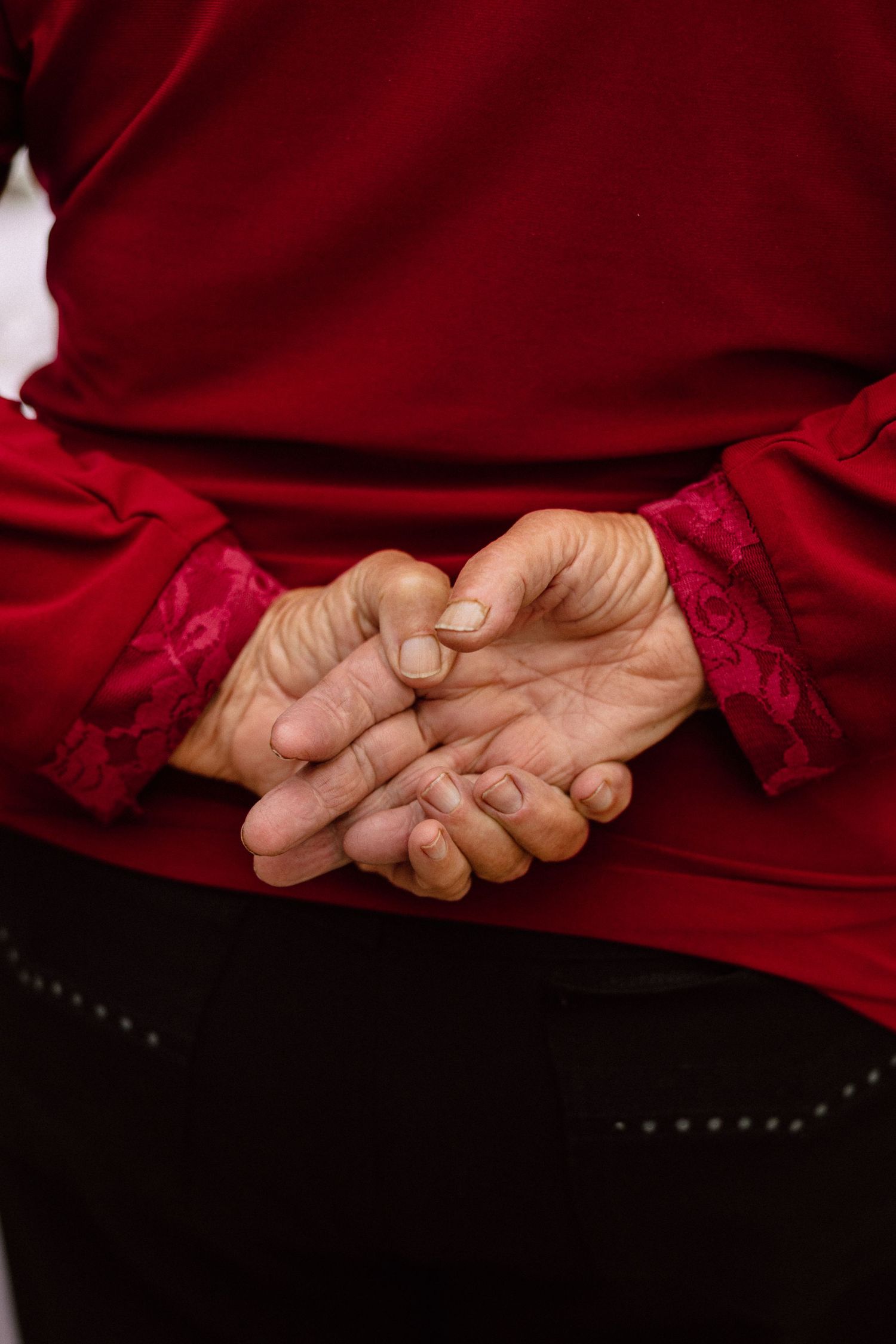 Hands clasped together against a deep red fabric background in an intimate gesture.