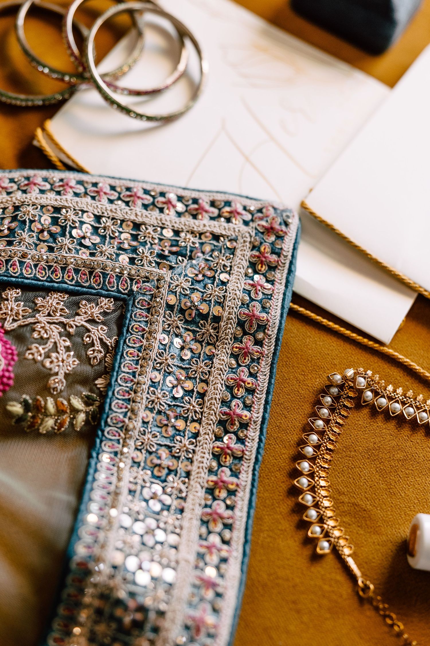 Intricate embroidered teal fabric with Indian bridal jewelry including bangles, earrings, and kundan necklace.