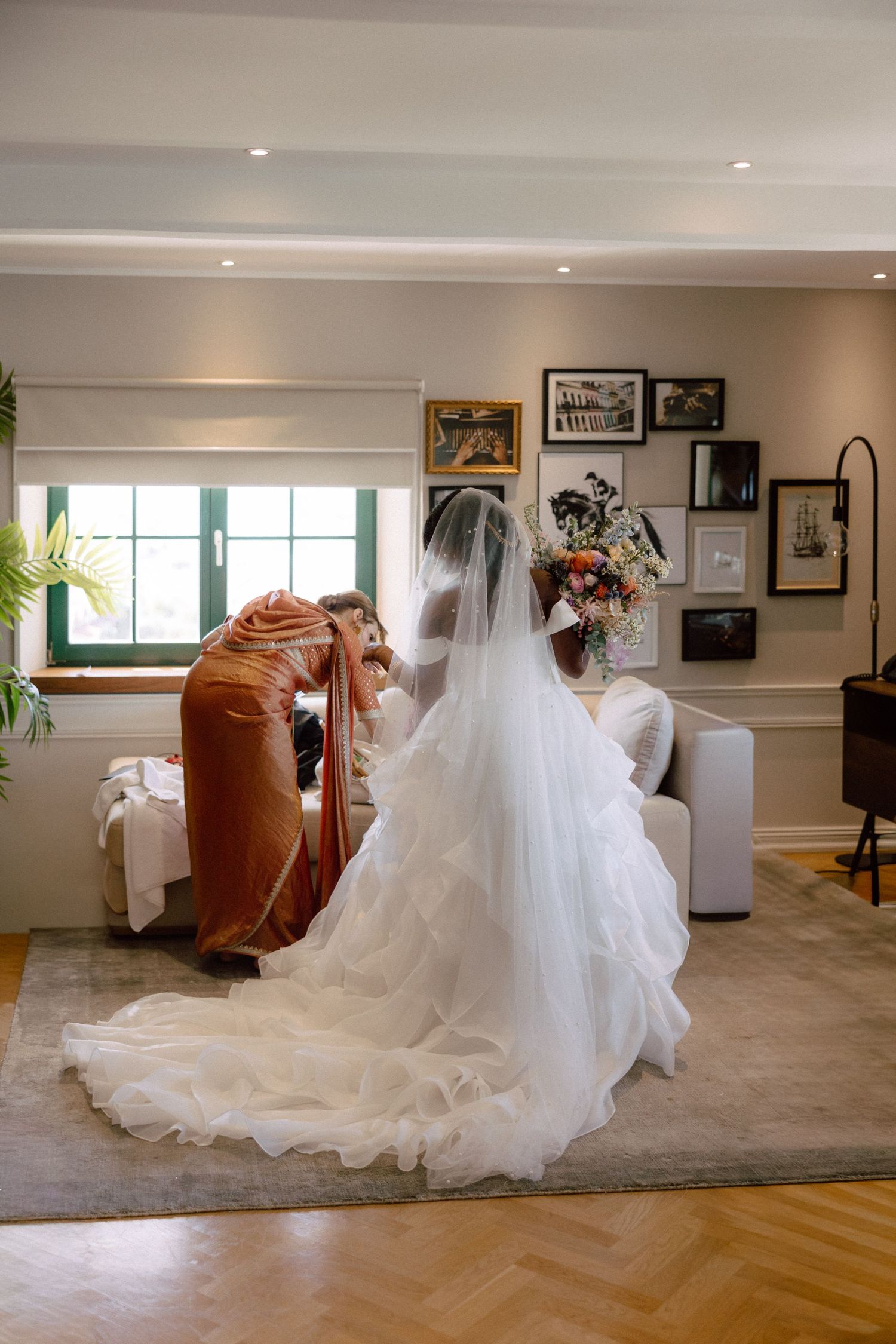Bride in ruffled wedding gown and veil with long train standing in elegant room holding a floral bouquet.