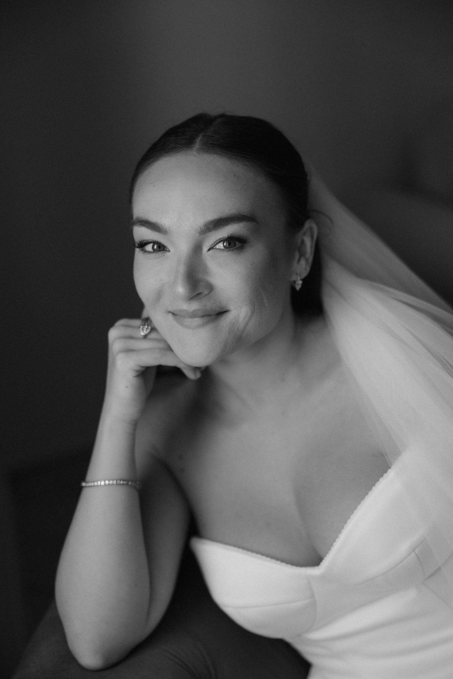 Stunning black and white bridal portrait of smiling bride in veil resting chin on hand.