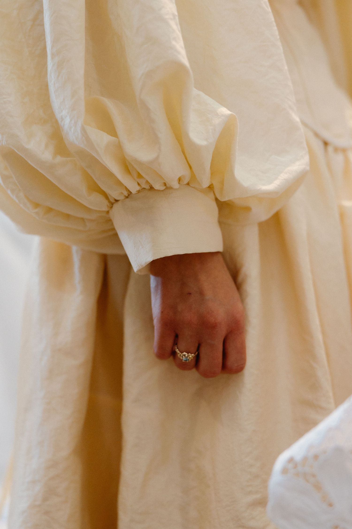 Detail shot of cream-colored dress sleeves and hands with an engagement ring.