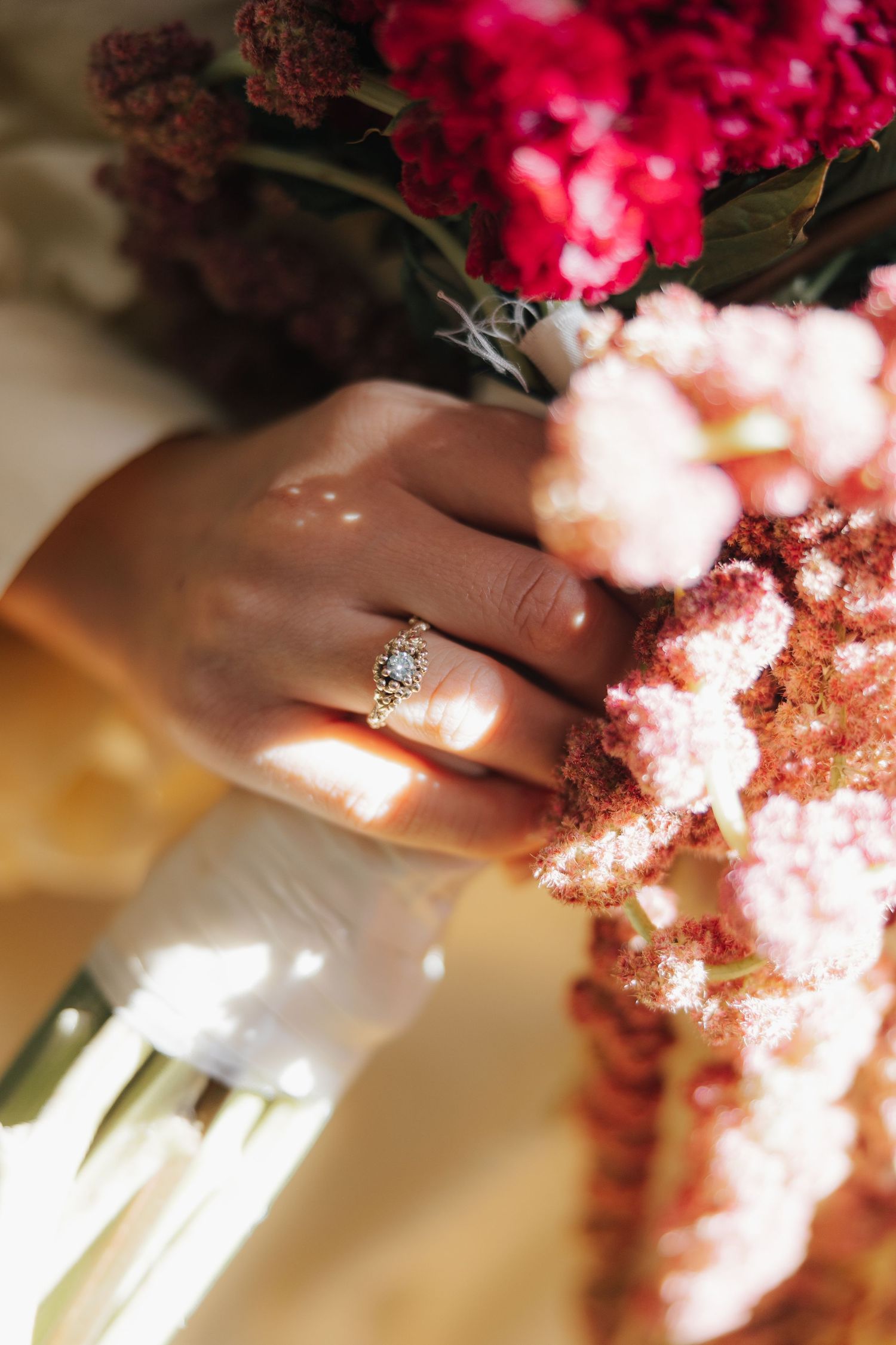 Close-up of an engagement ring with pink and red flowers in soft natural lighting.