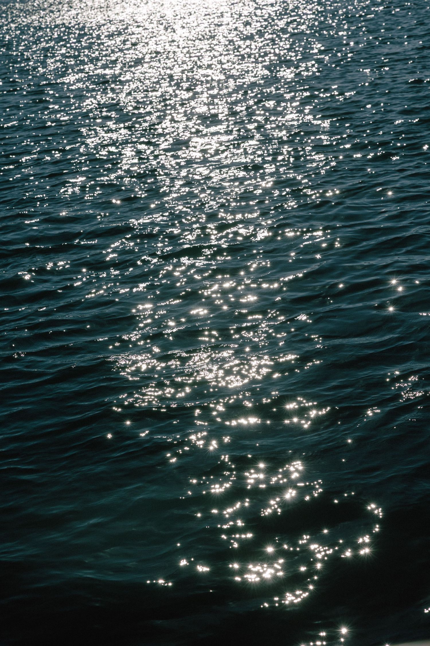 Sunlight sparkles on dark rippling ocean water creating beautiful glittering reflections.