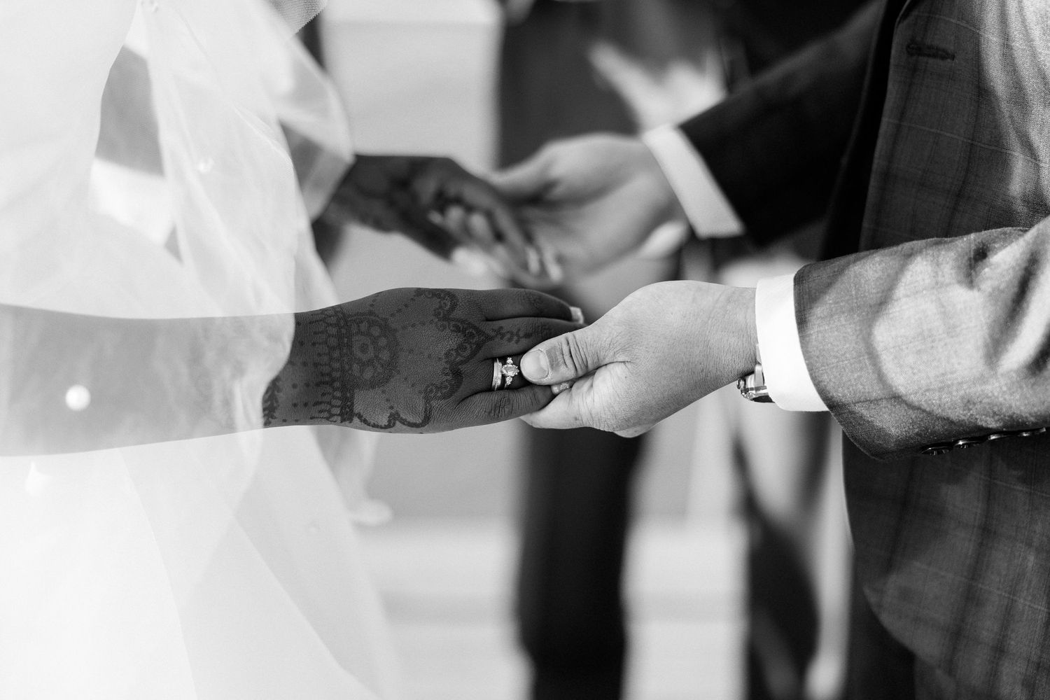 Black and white close-up of a groom placing a wedding ring on the bride's finger during the ceremony.
