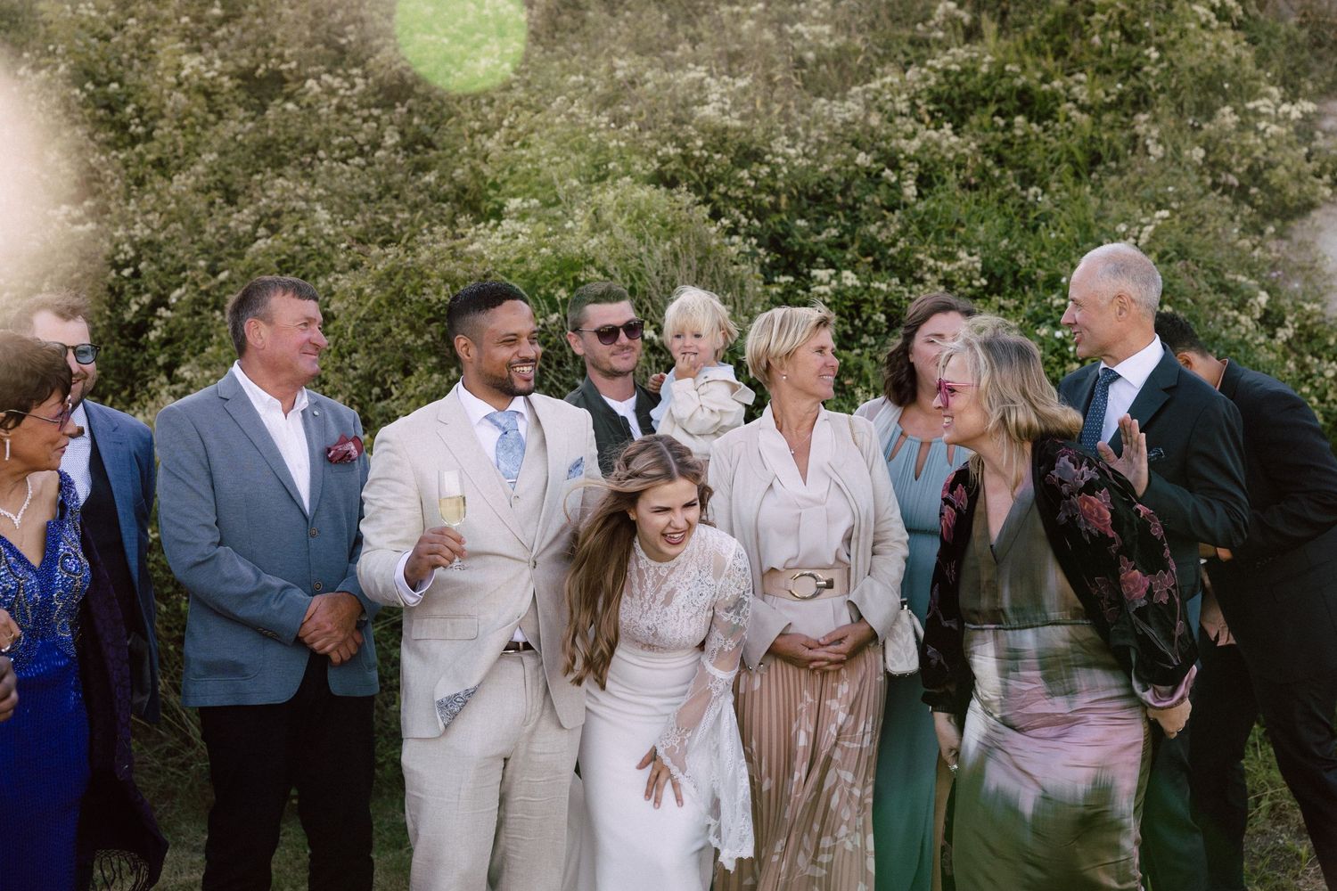 Wedding party gathered outdoors sharing laughs in formal attire.