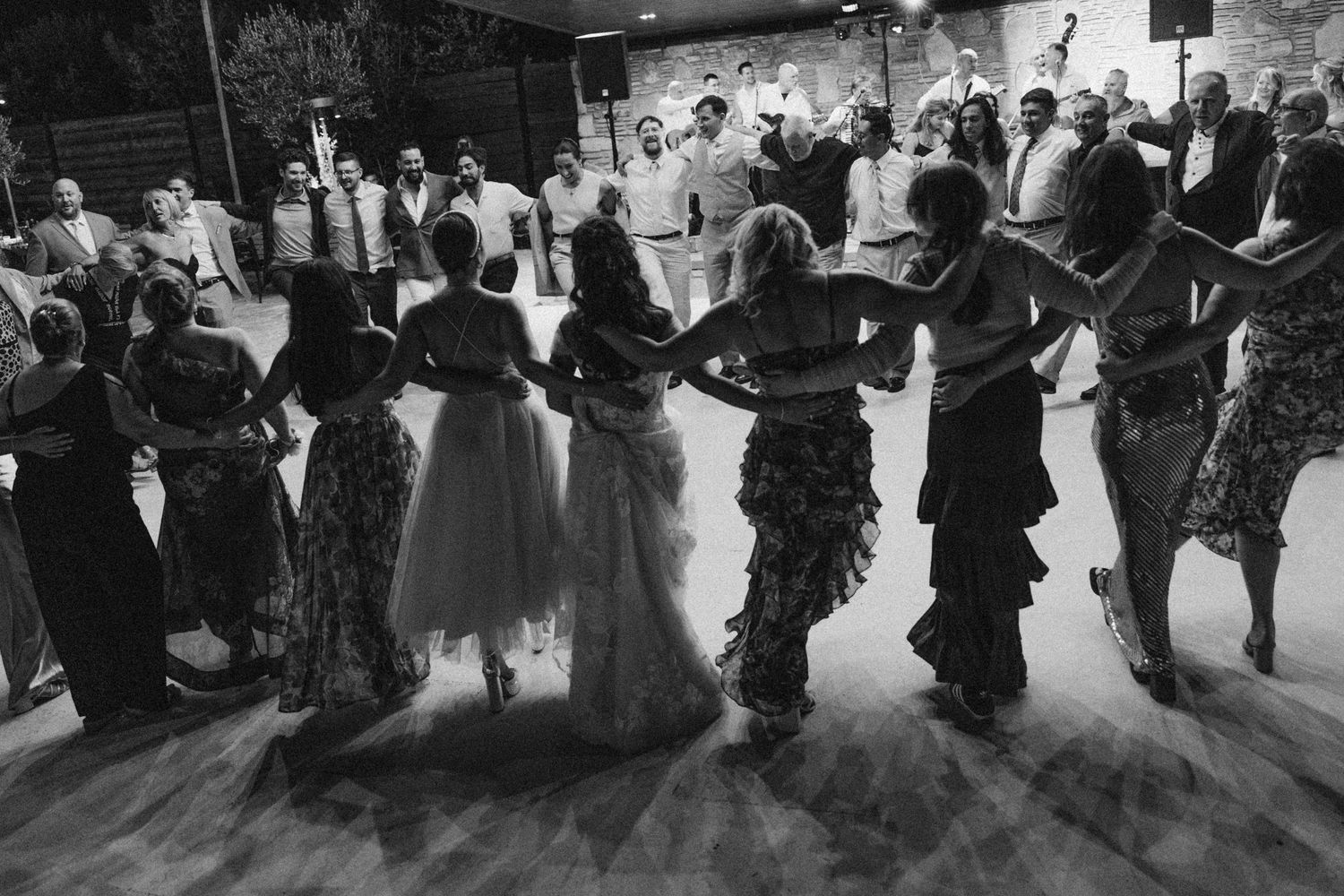 Large group of wedding guests form a line for traditional dance at reception.