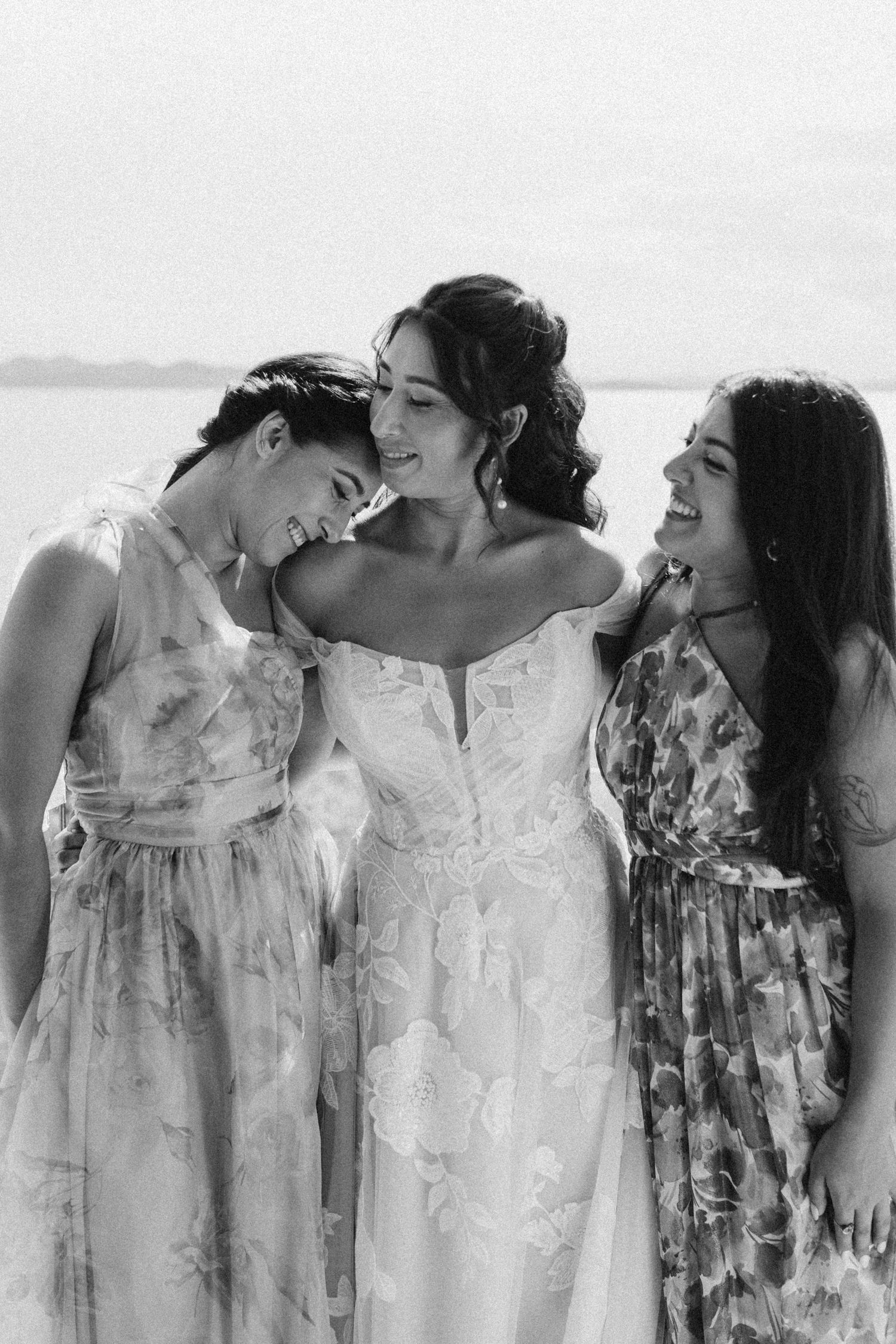 Row of bridesmaids in light floral dresses sharing candid moment.