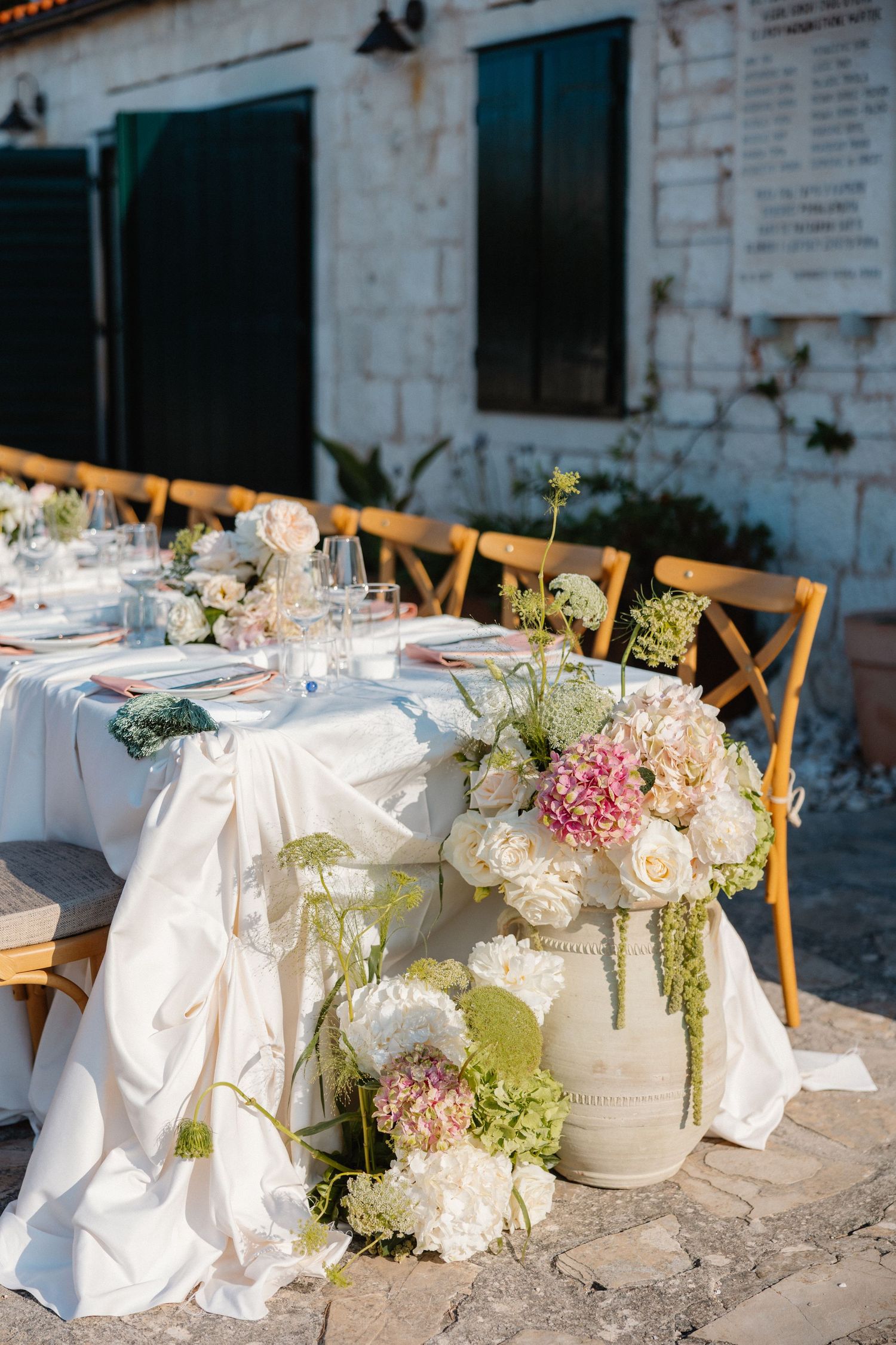 Outdoor wedding reception table with white linen and pink hydrangea floral centerpiece.