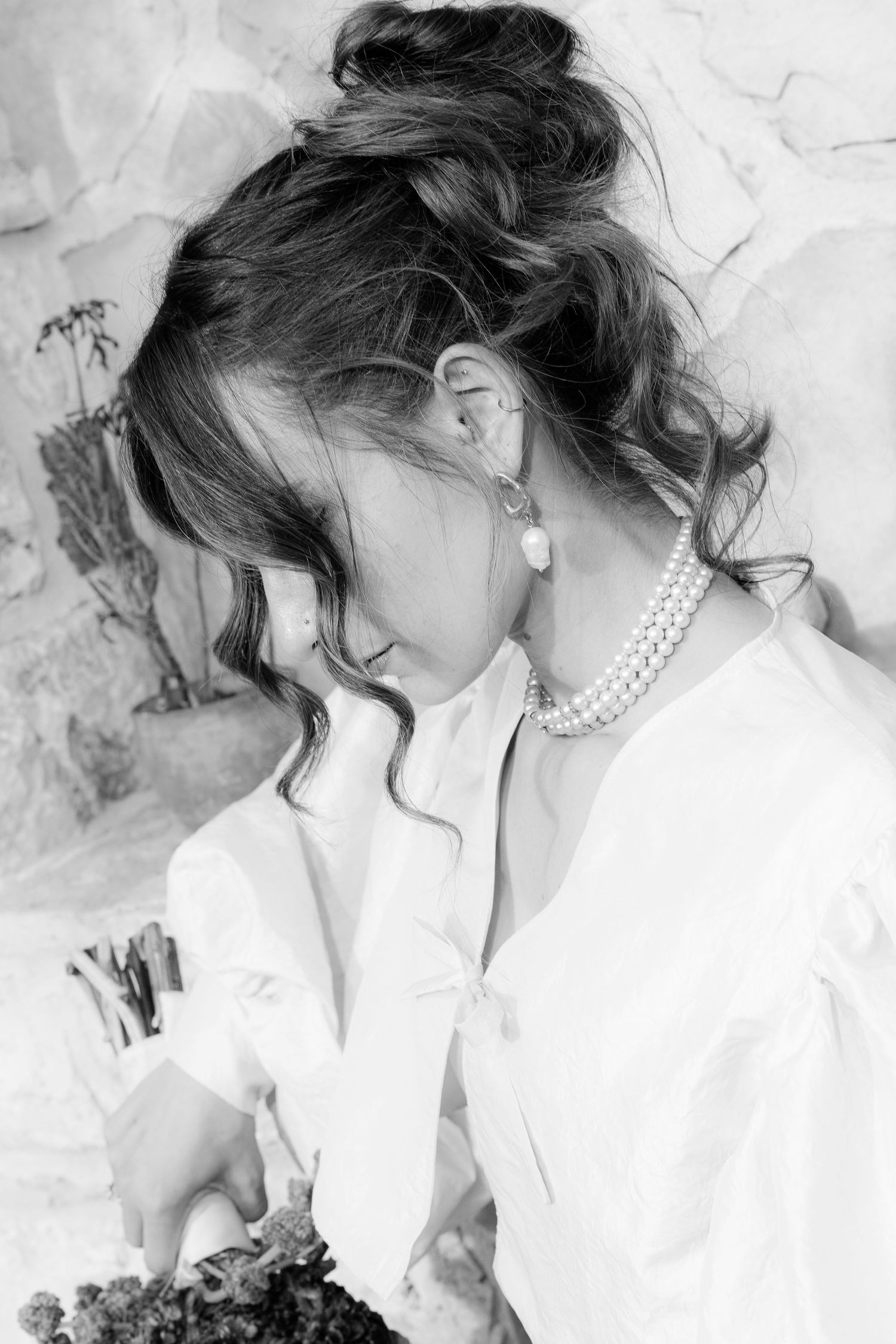 Elegant portrait featuring pearl necklace and white blouse against light background.