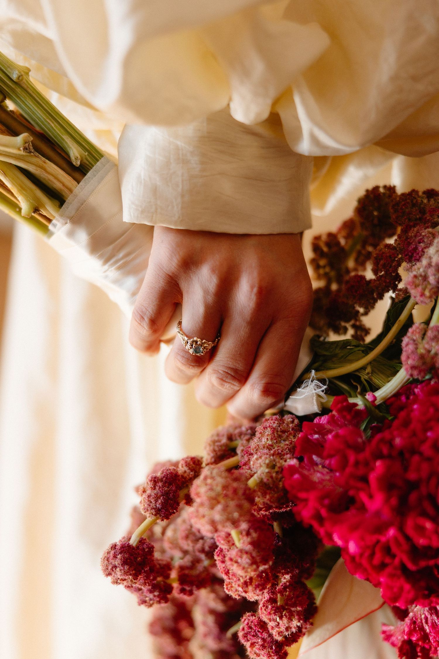 Hands holding vibrant pink and burgundy flowers with rings visible.