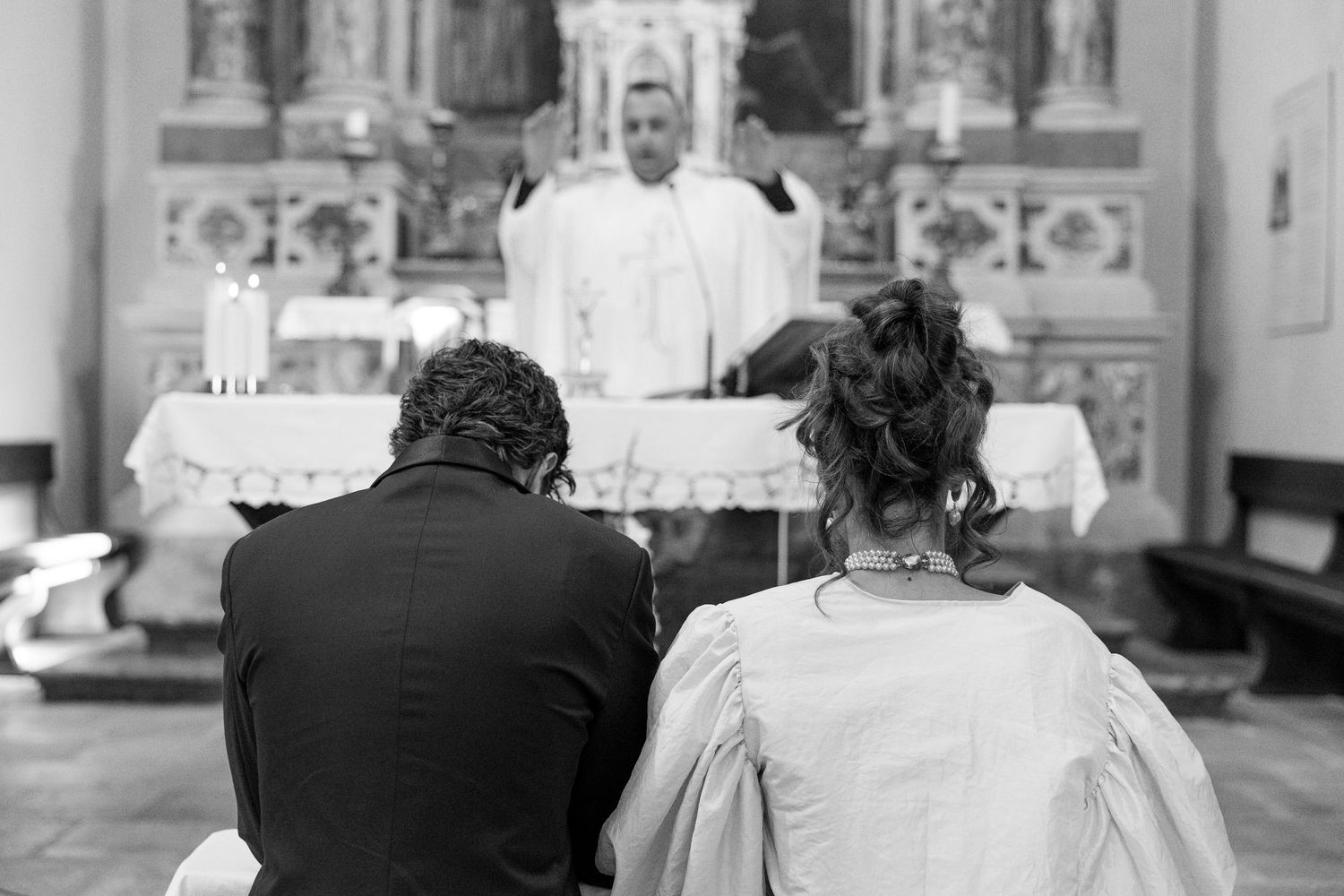 Black and white photo of church pews and decorative interior during a ceremony.