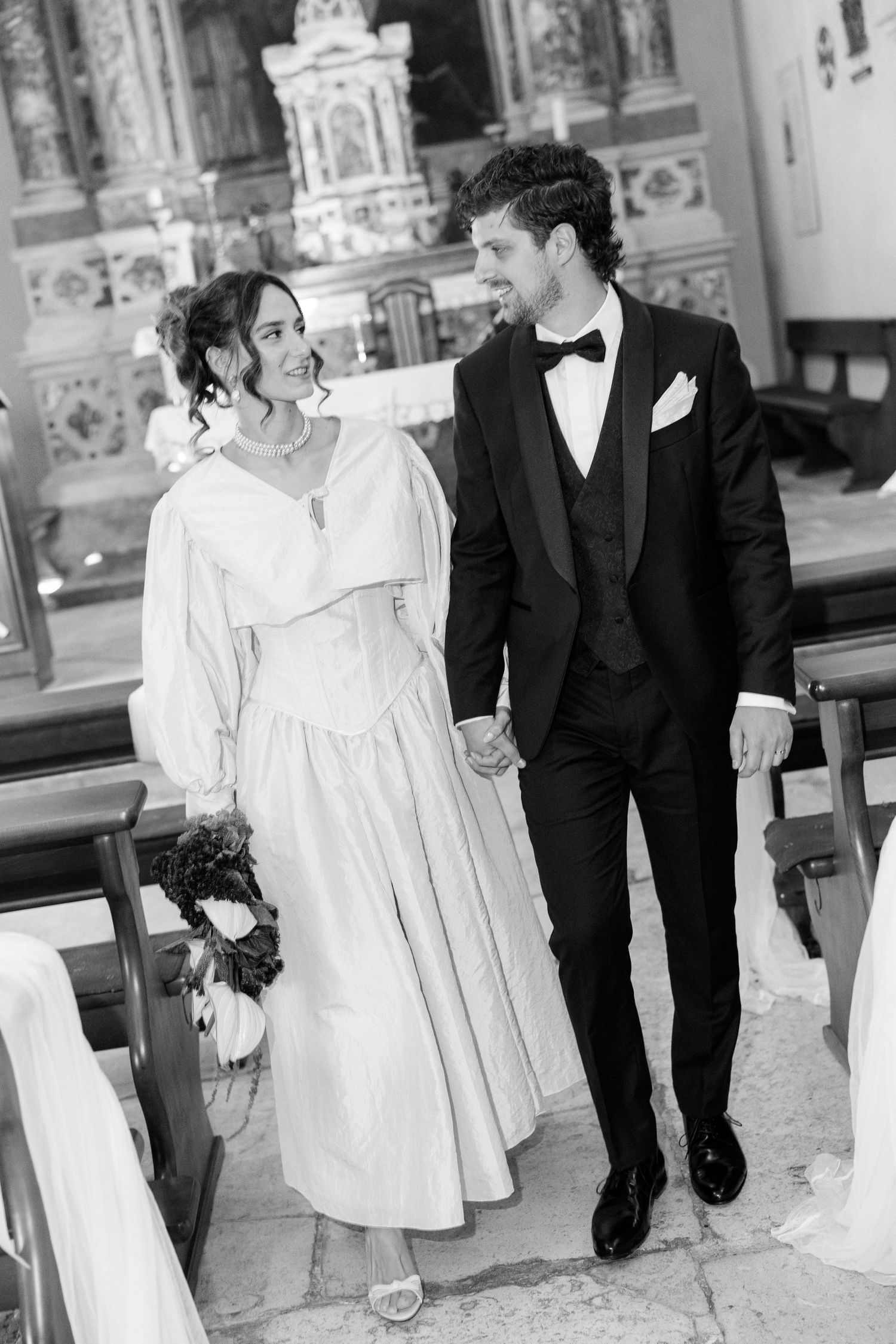 Couple walking together in formal wedding attire in black and white.