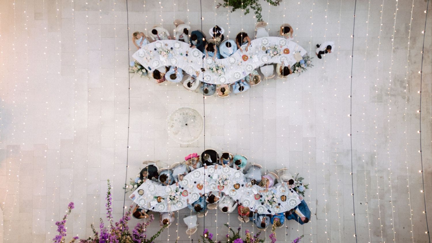 Overhead view of people sitting in curved rows on a white floor with twinkle lights in the background.