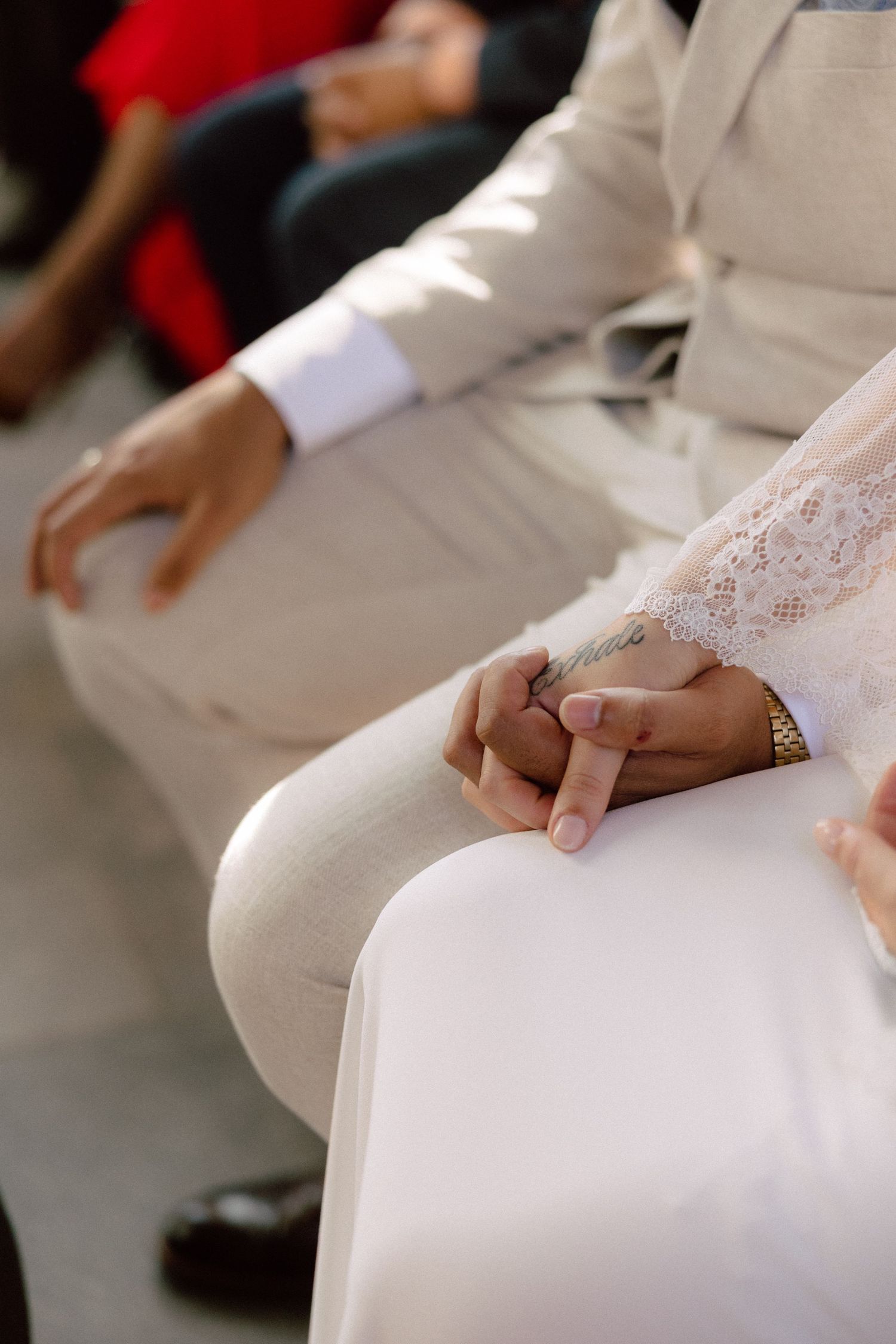 Close-up of couple holding hands while seated during wedding ceremony.