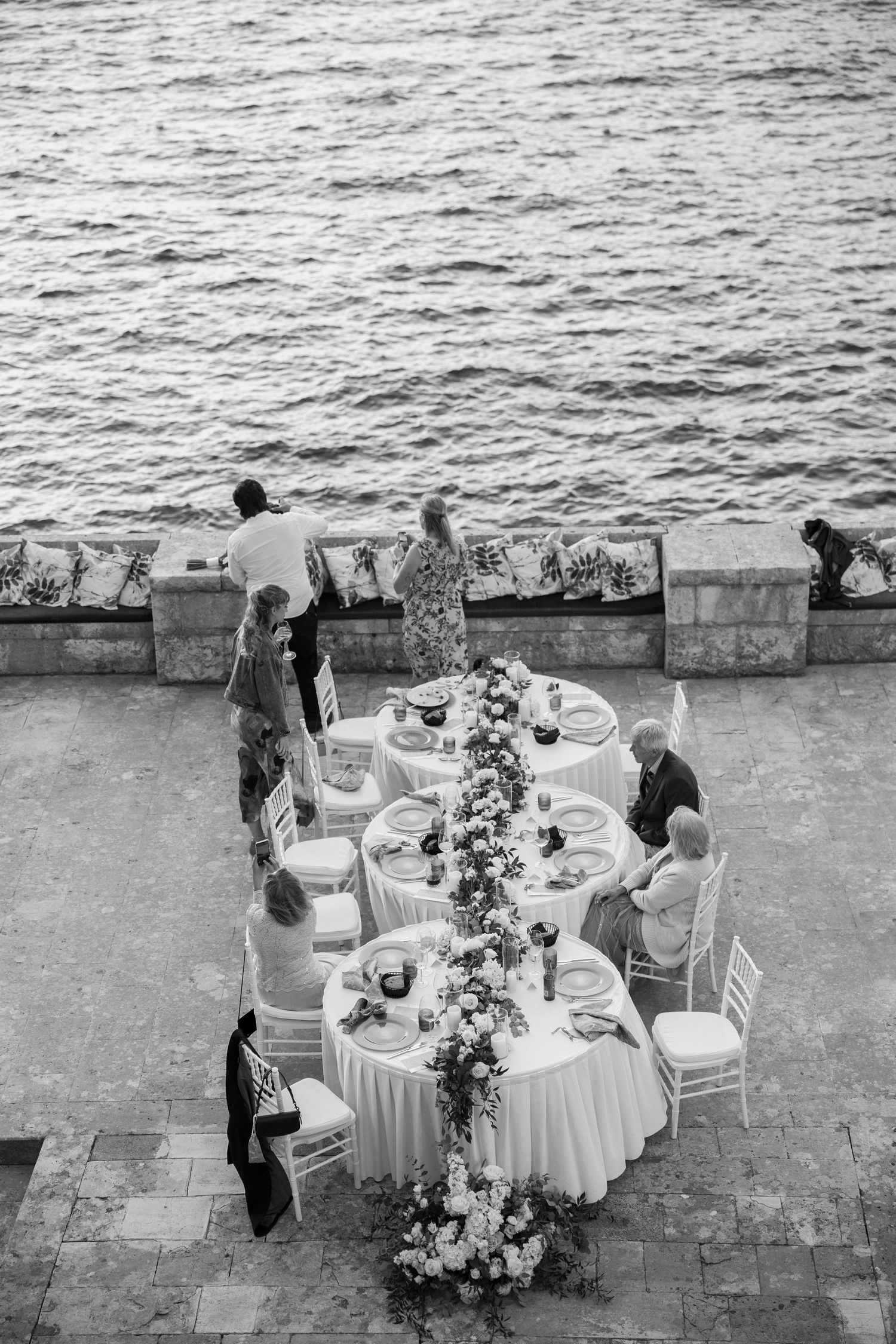 Elegant outdoor wedding reception tables set up by the ocean with white linens and floral centerpieces.