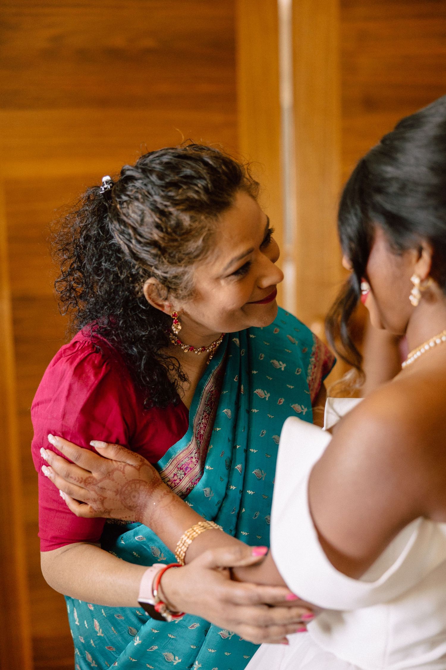 A woman in a teal saree tenderly holds a bride's hands while sharing an emotional moment before the wedding ceremony.