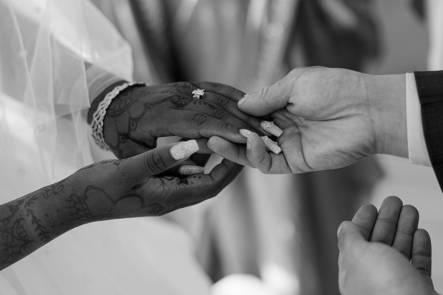 Close-up black and white photo of hands exchanging wedding rings during a marriage ceremony.