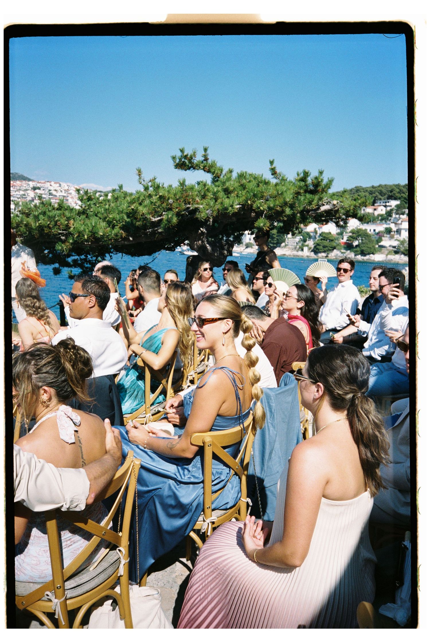 Wedding guests seated outdoors by the sea on a sunny Mediterranean day.