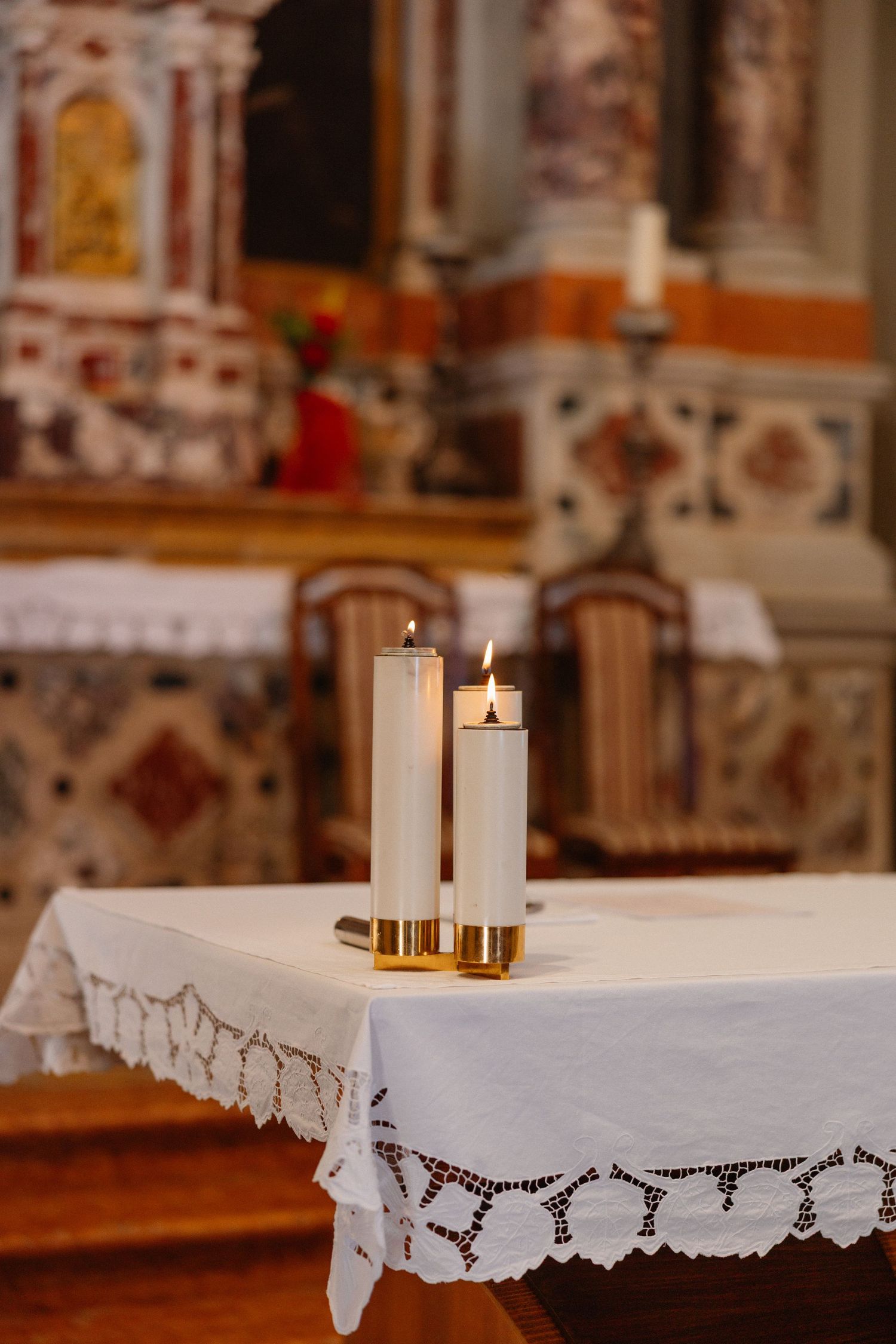 White lace tablecloth with lit candles on altar in church sanctuary.