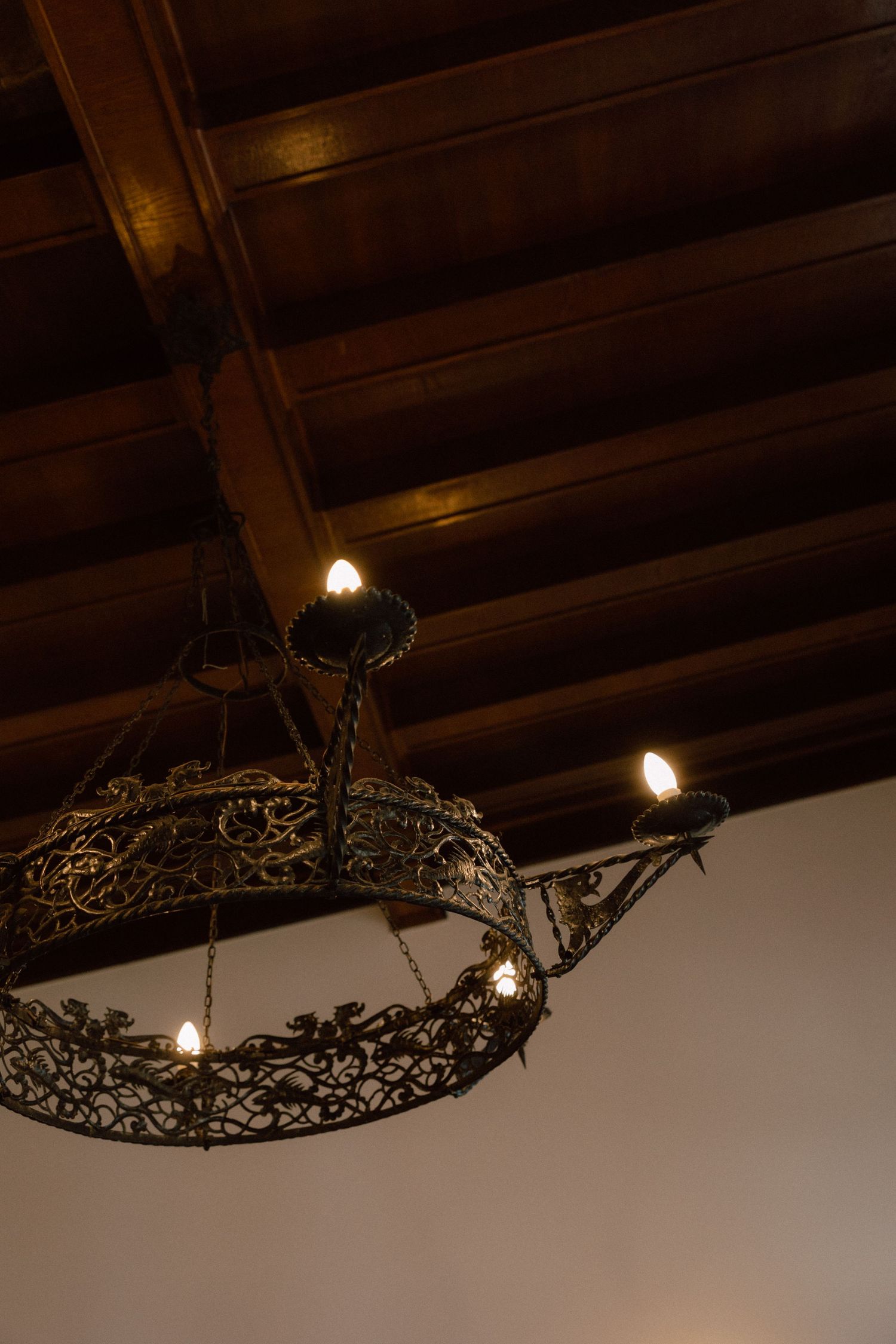 Ornate wrought iron chandelier with intricate patterns hanging from wooden beamed ceiling.