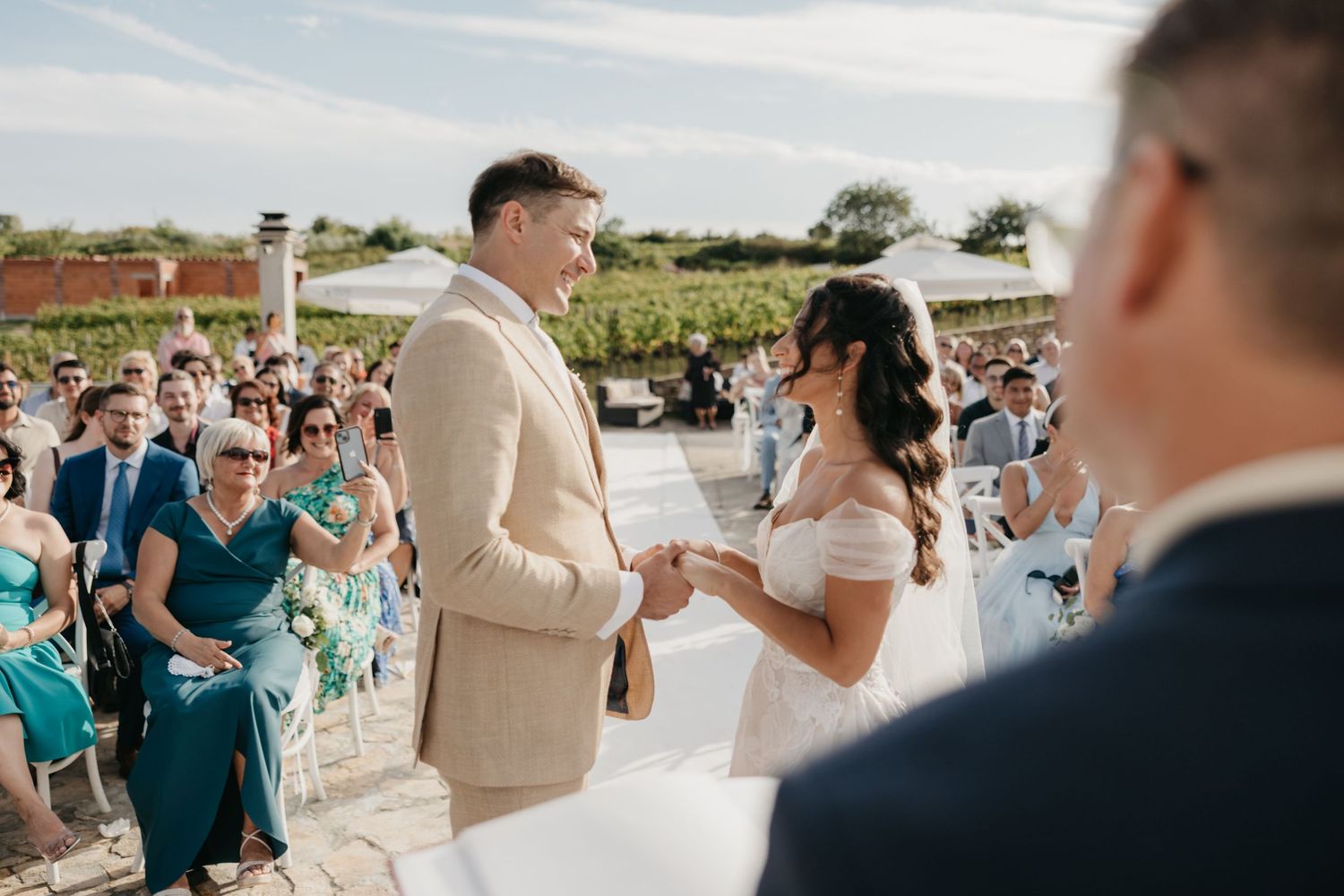 Wedding guests gather outdoors to celebrate and take photos during a sunny celebration.