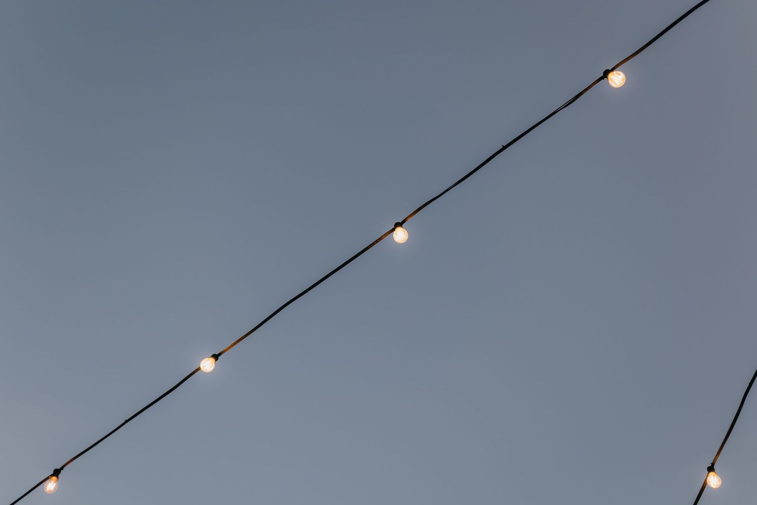 String lights hang against a dusky blue sky creating a romantic outdoor ambiance.