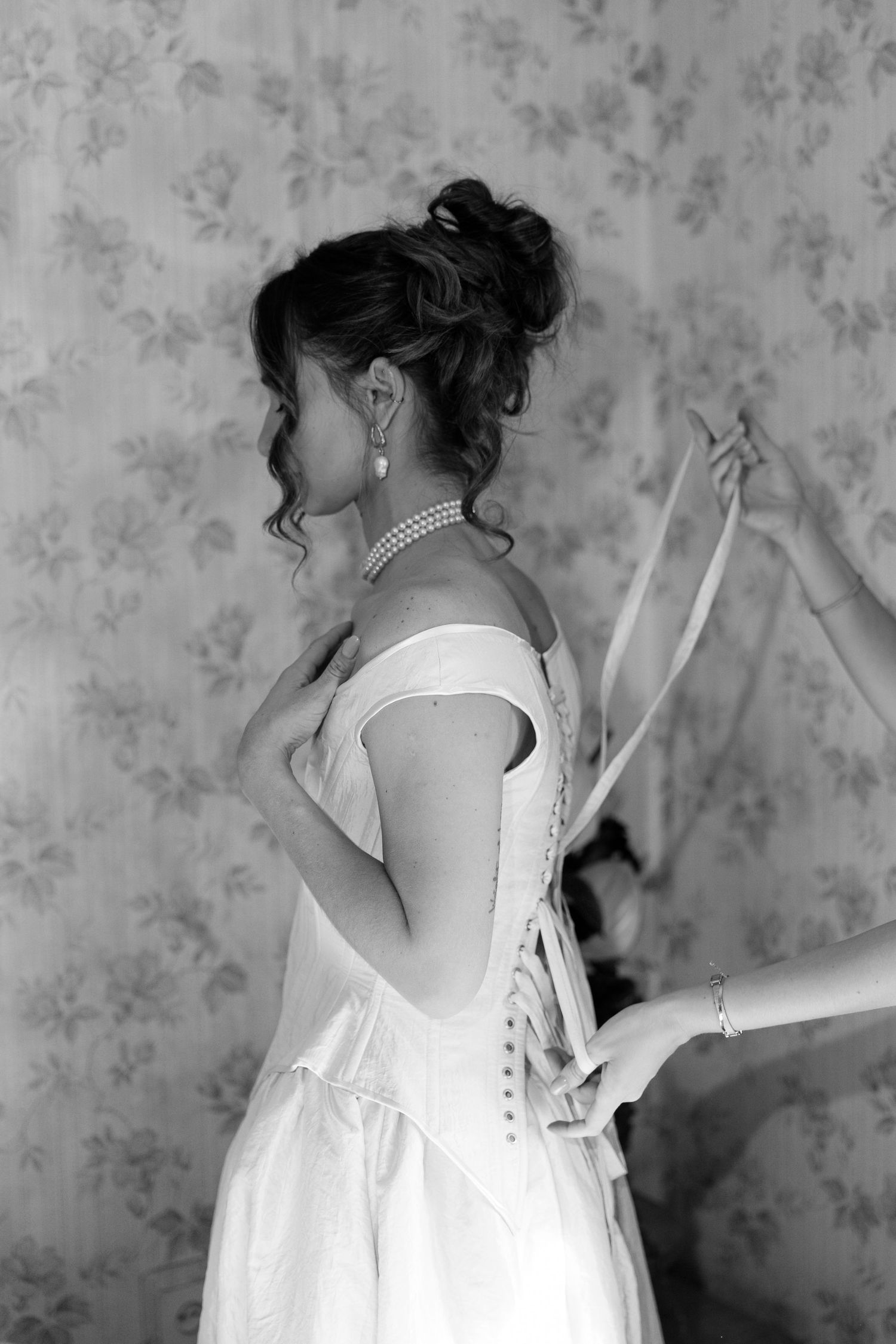 Black and white photo of bride getting laced into wedding dress.