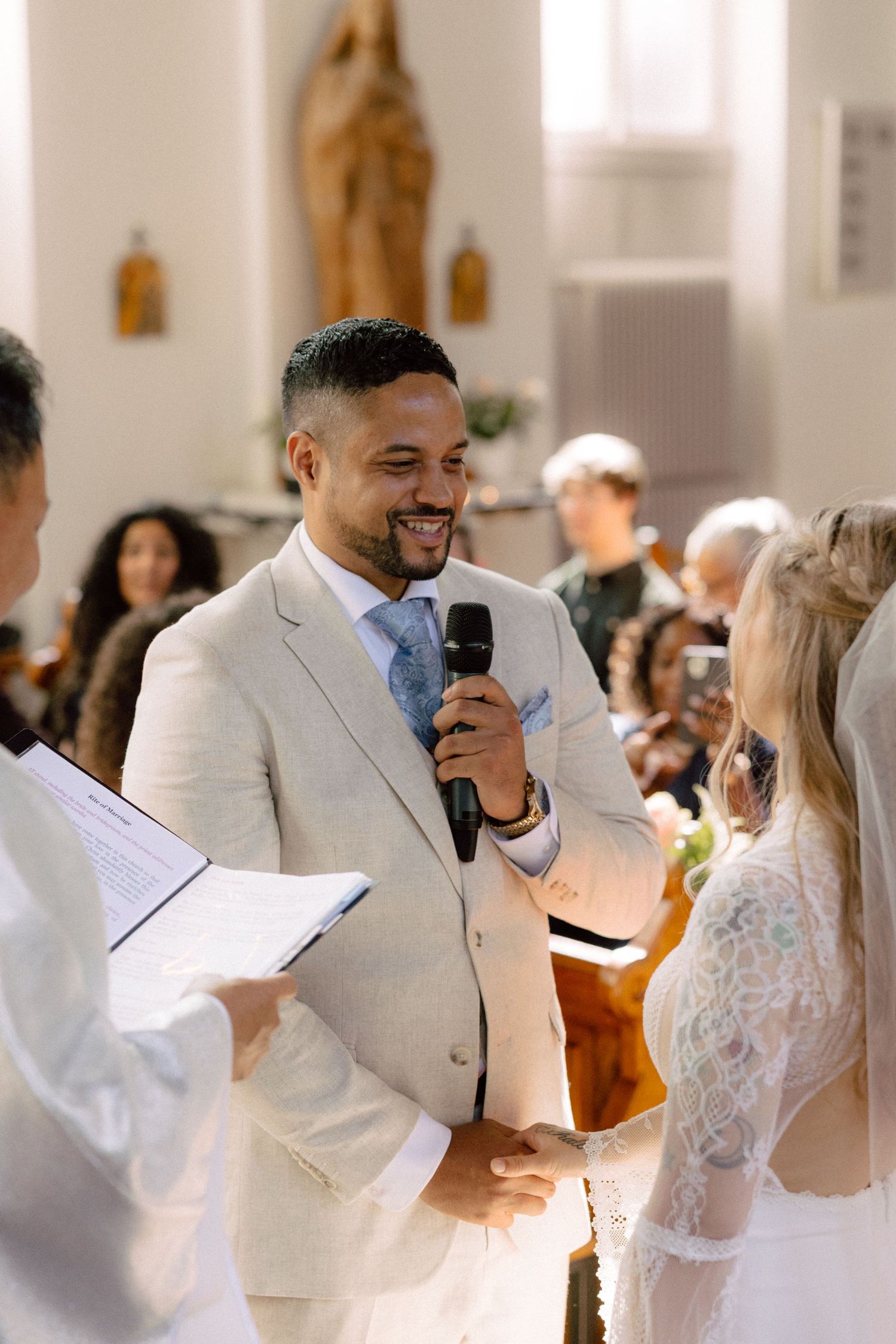A couple exchanges vows during their wedding ceremony in a church with the groom speaking into a microphone.