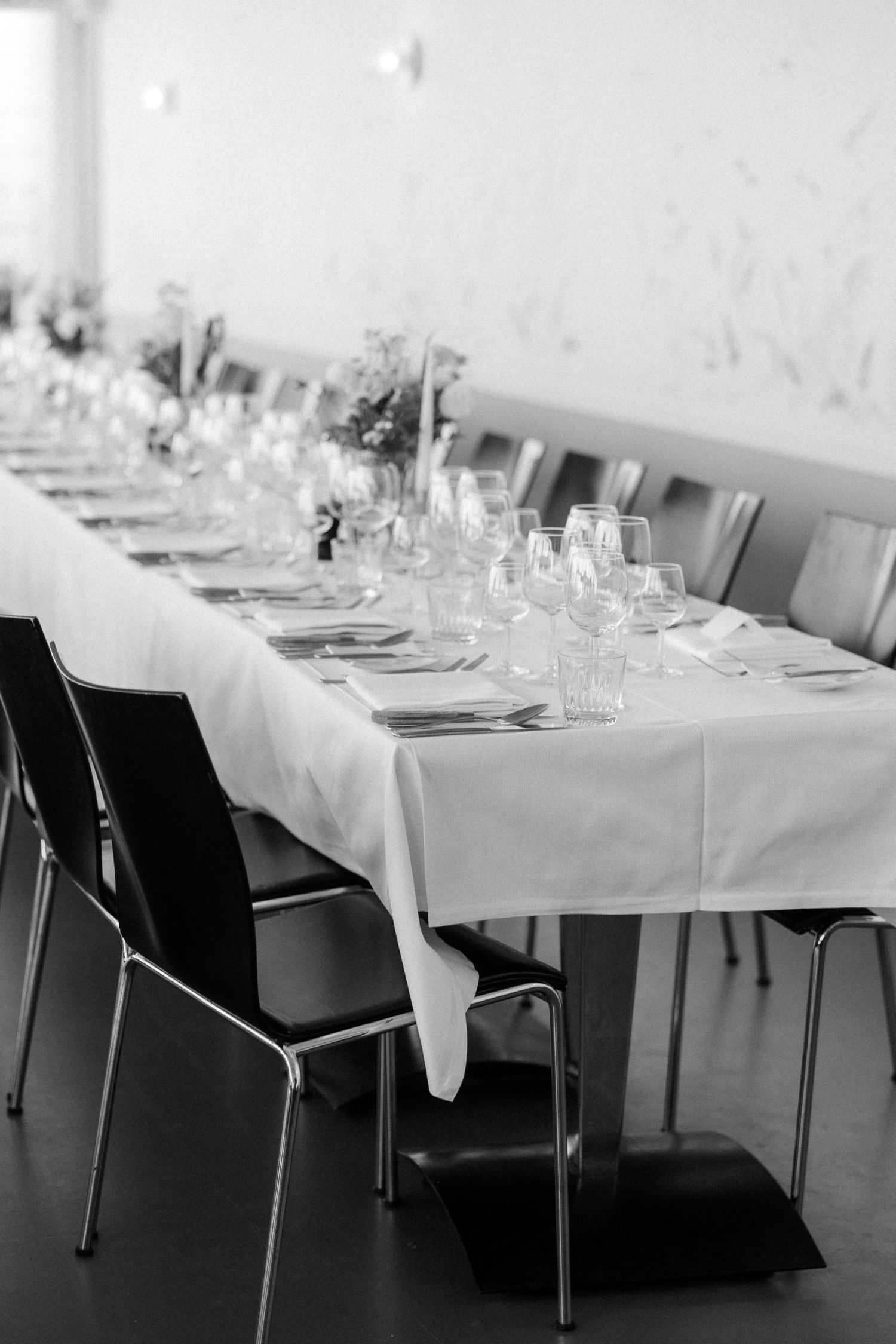 Long elegant dining table set with white linens and glassware for a formal event.