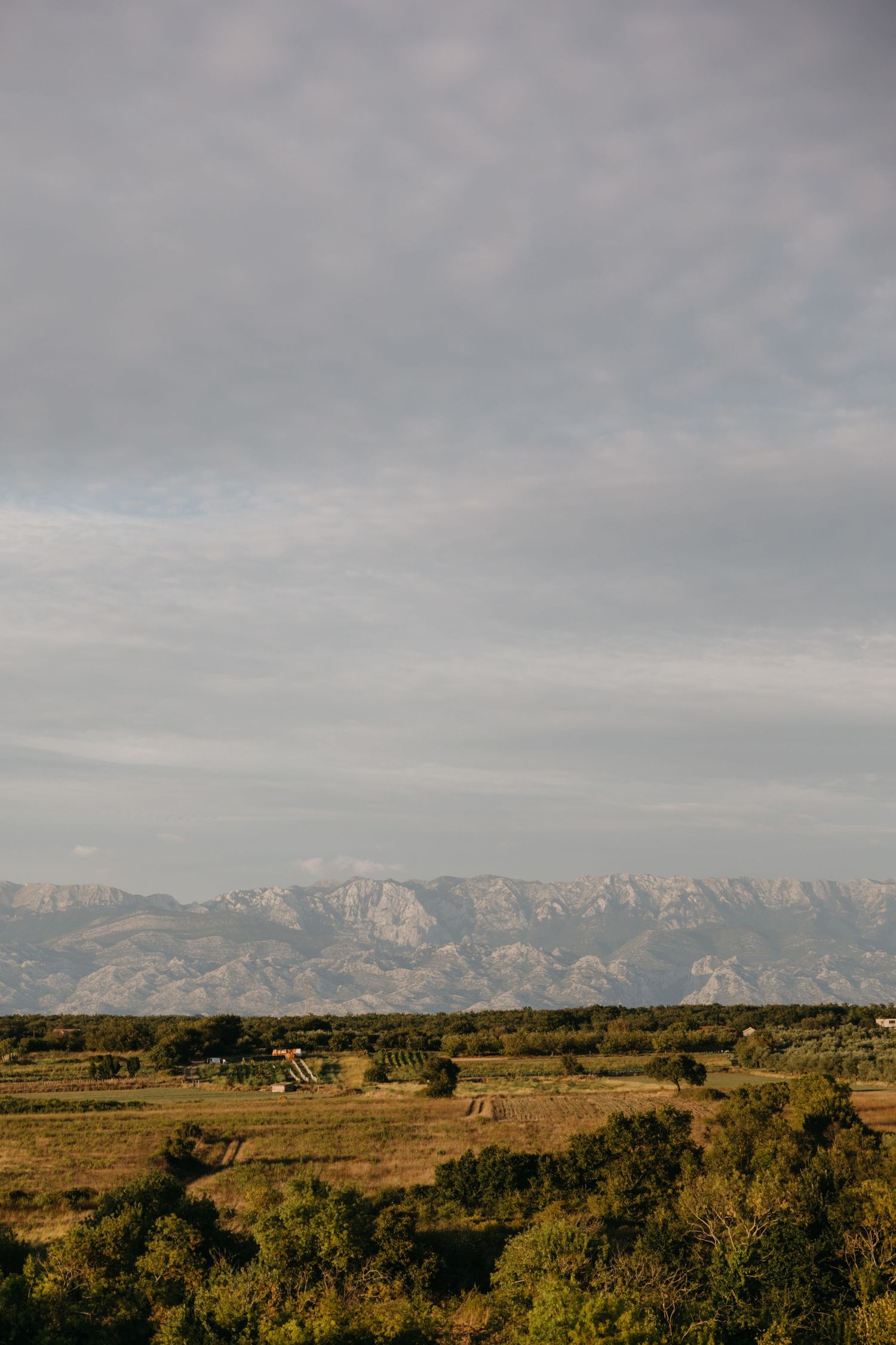 Rolling hills and mountains extend across a scenic landscape under cloudy skies.