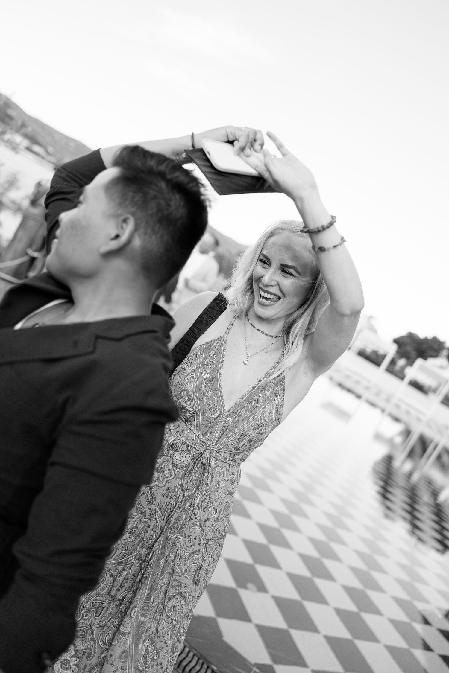 Black and white photo of laughing blonde woman being twirled by partner on checkered dance floor.