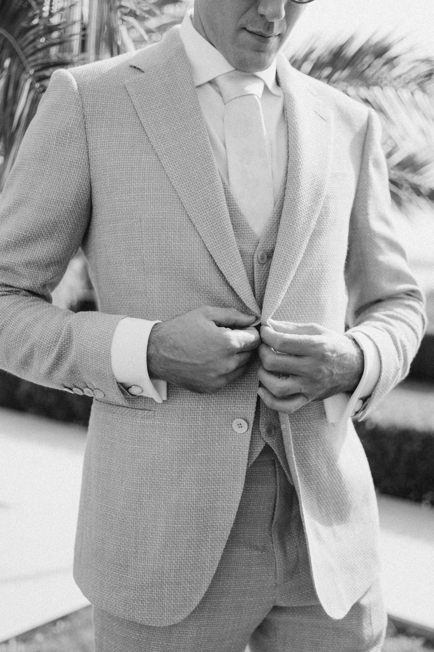 Close-up black and white photo of groom adjusting light gray suit jacket.