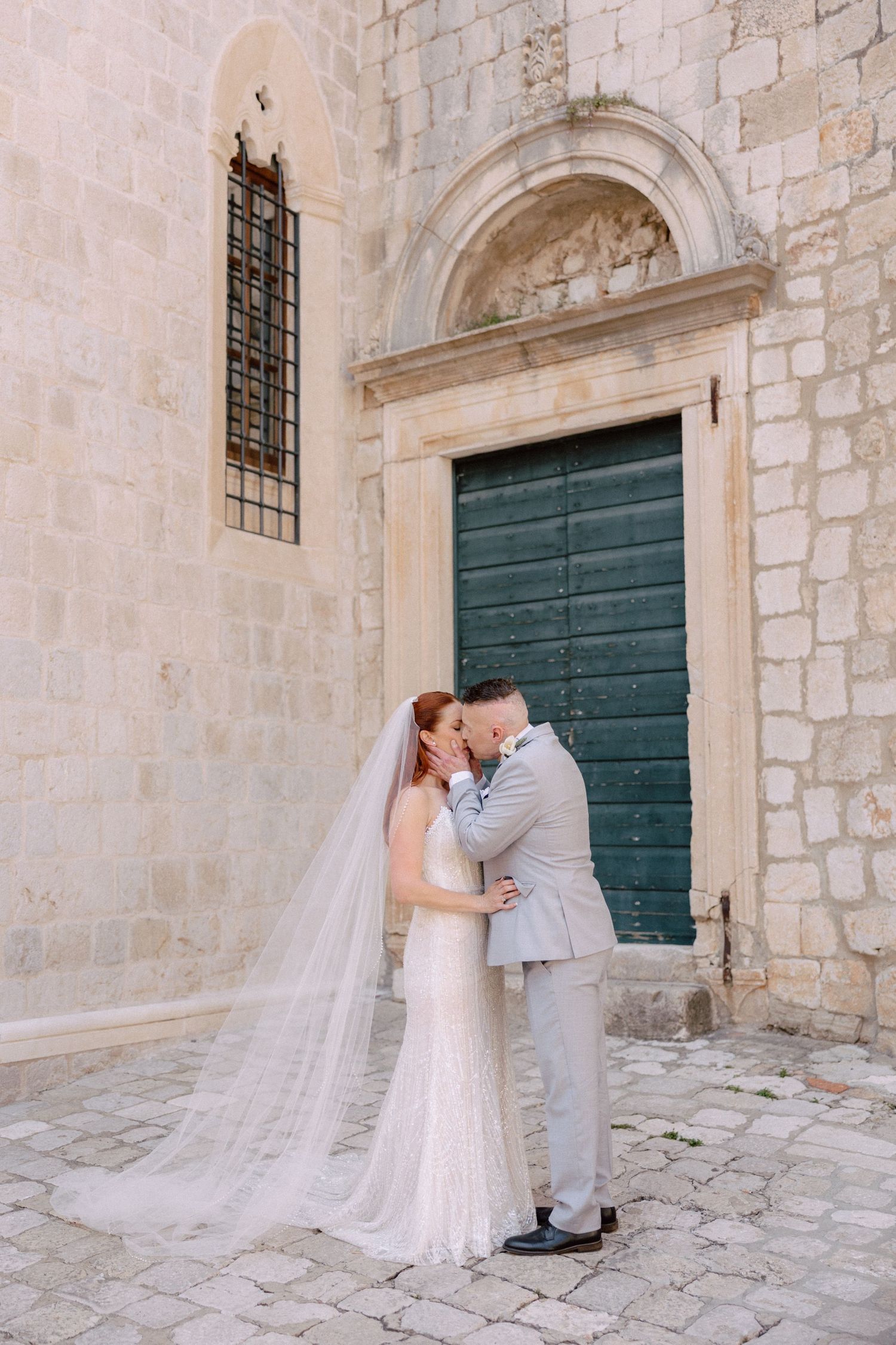 Romantic wedding photos against an ancient stone wall with dark green wooden doors.