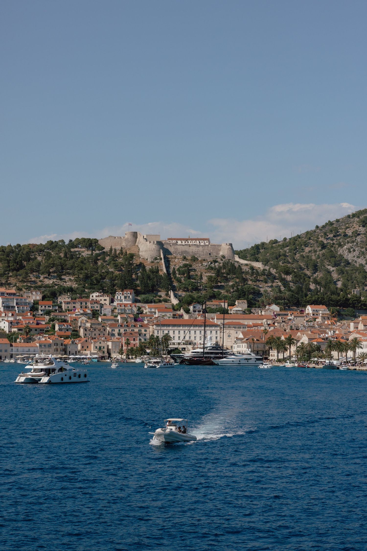 Scenic coastal town of Hvar Croatia with fortress on hilltop and boats in blue harbor.