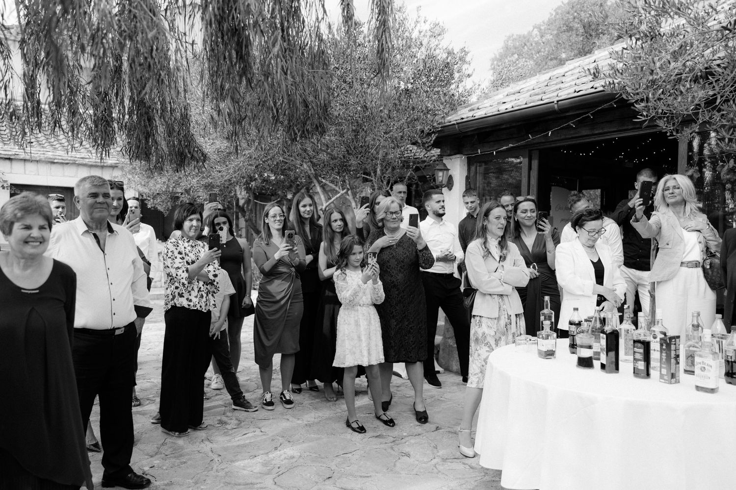 Black and white photo of outdoor wedding gathering with guests lined up under trees.