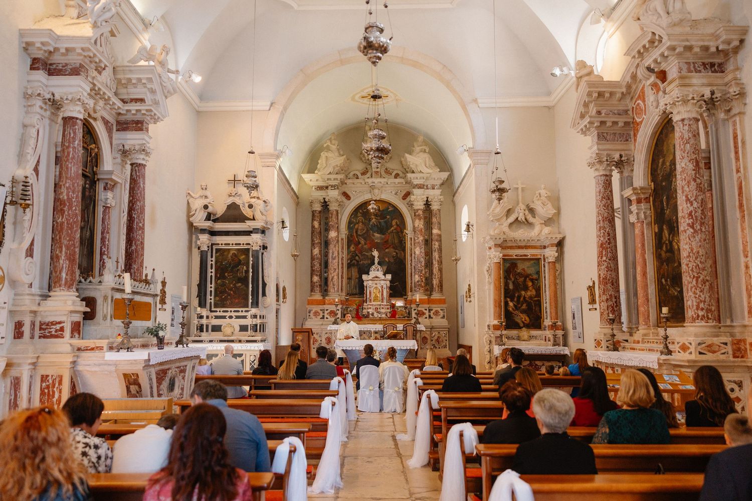 Interior of ornate church with white arched ceilings and decorative altars.