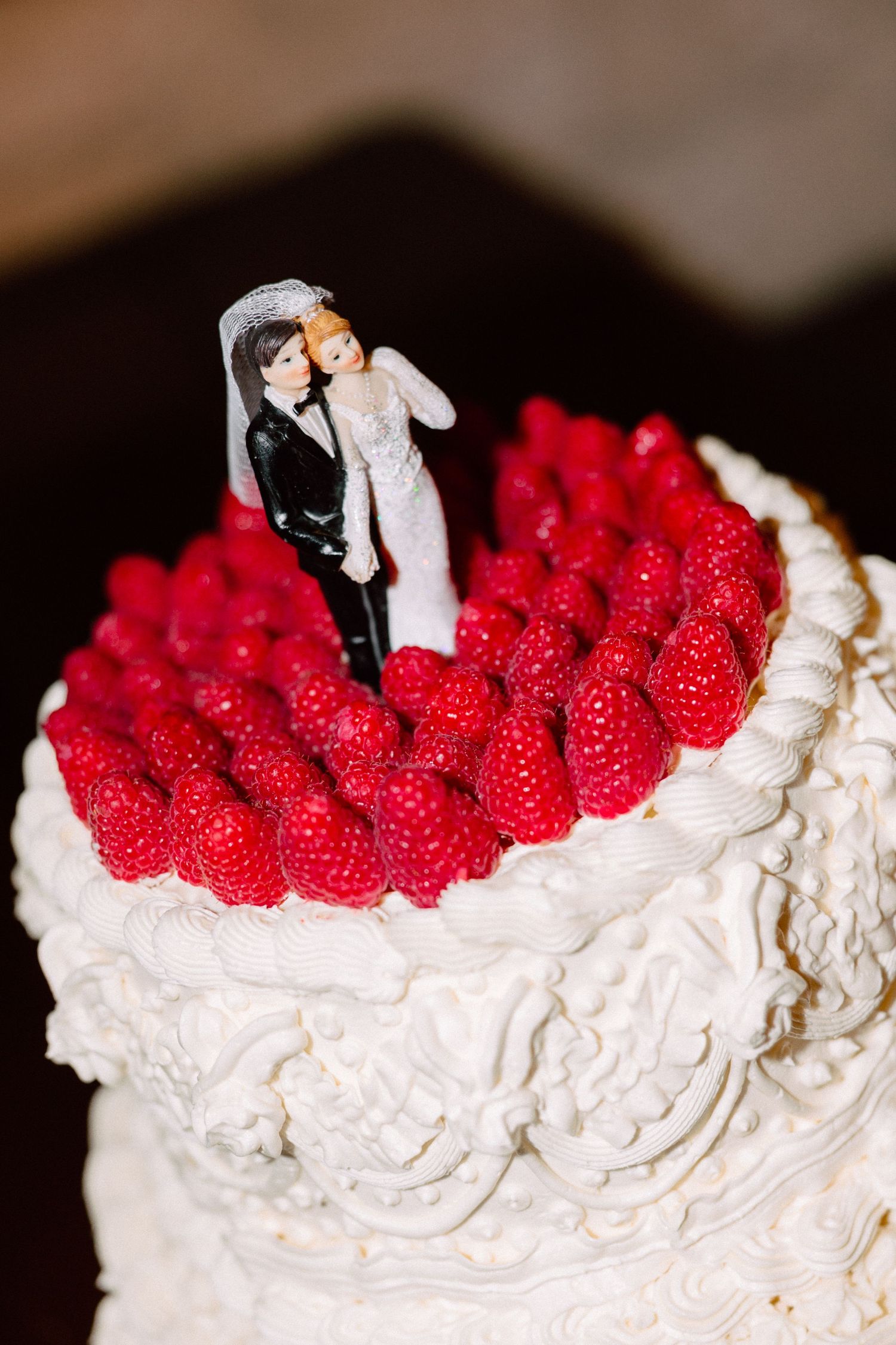 Wedding cake topper decorates white frosted cake with fresh red raspberries arranged on top.