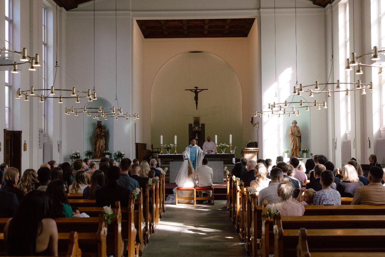 Interior of a bright church sanctuary with chandelier lighting and wooden pews.