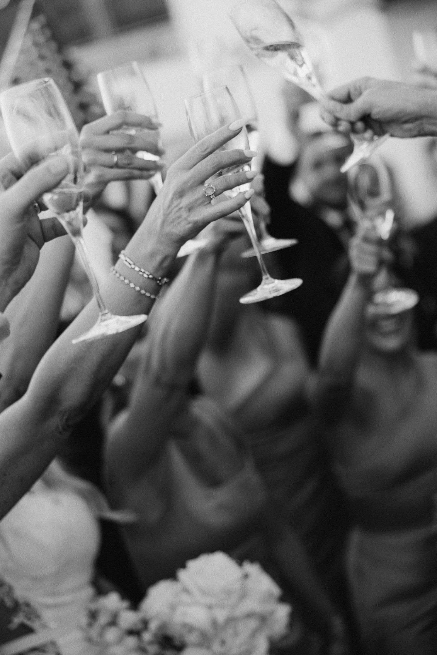 Black and white shot of guests raising champagne glasses in celebration.