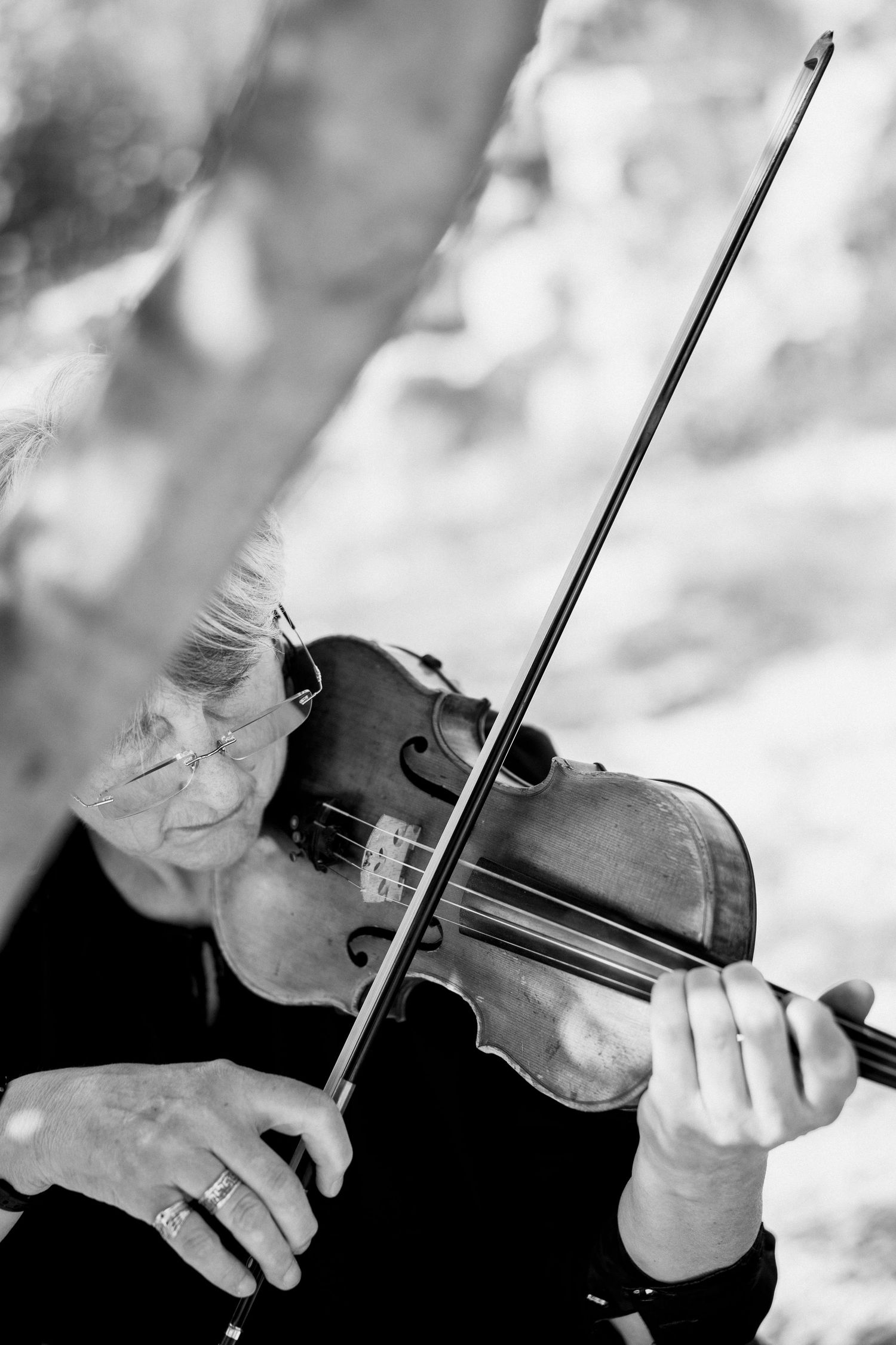 Close-up black and white shots of hands playing a violin during a wedding ceremony.