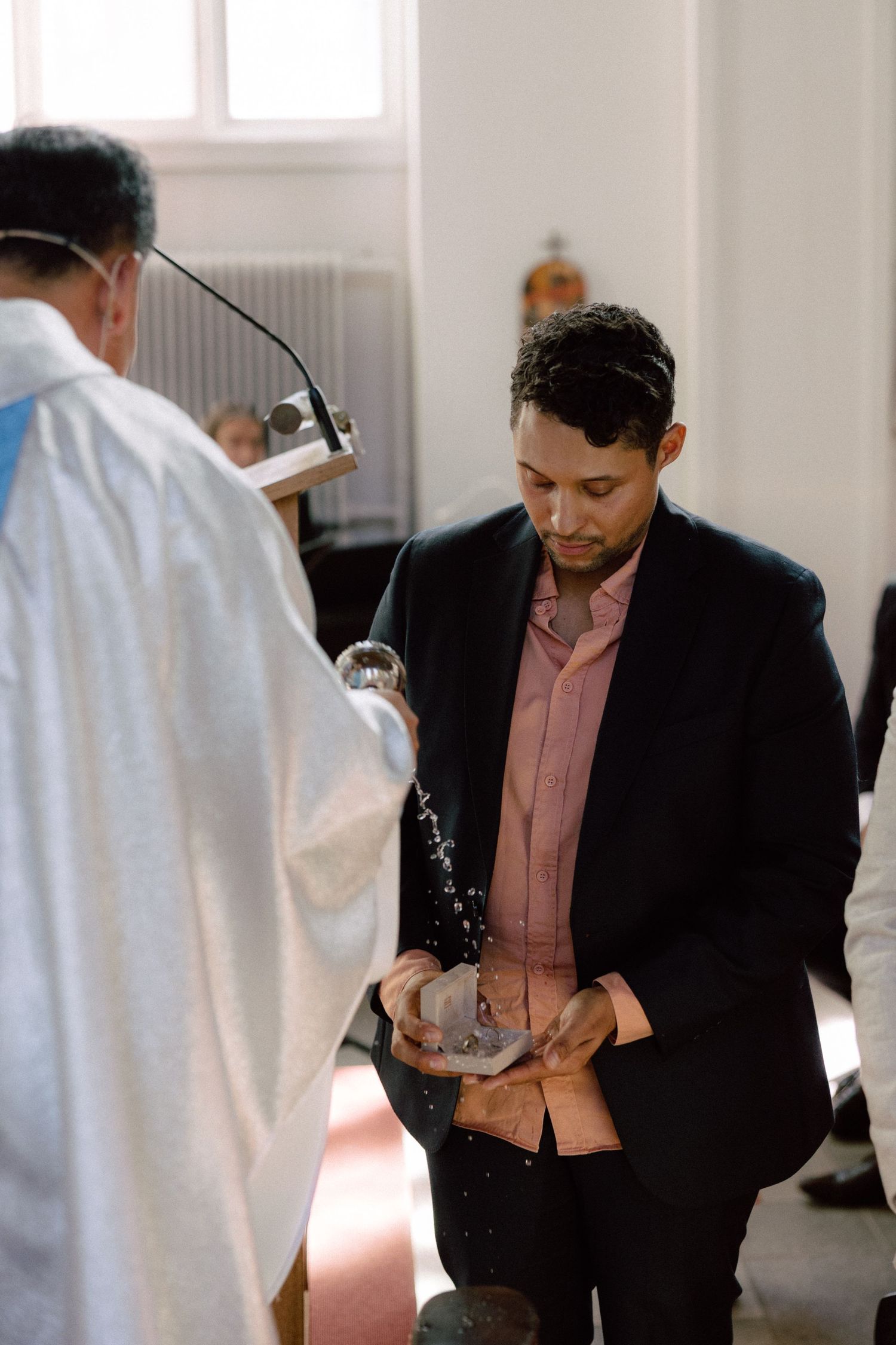 Person receiving holy water blessing from priest during religious ceremony in church.