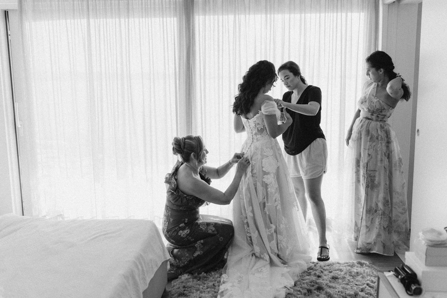 Wedding preparations with bridesmaids helping with dress.
