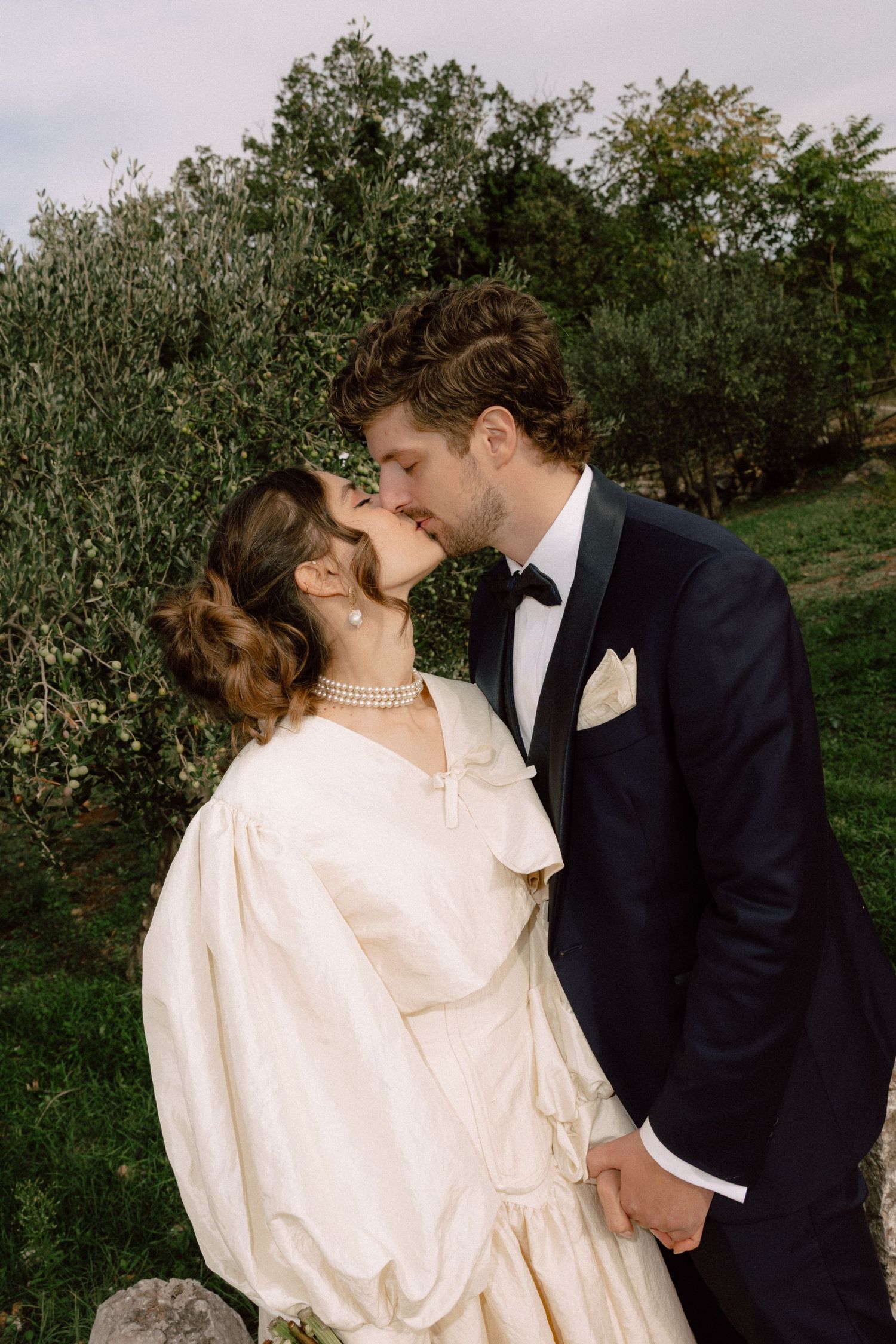 A romantic outdoor wedding photoshoot in an orchard featuring an elegant vintage-style cream dress.