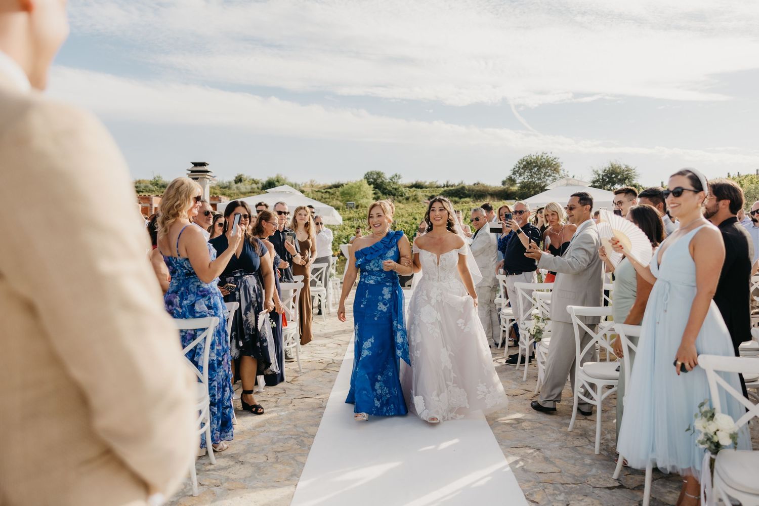 Wedding guests seated in white chairs on a sunny day with floral arrangements and decor in Italy.